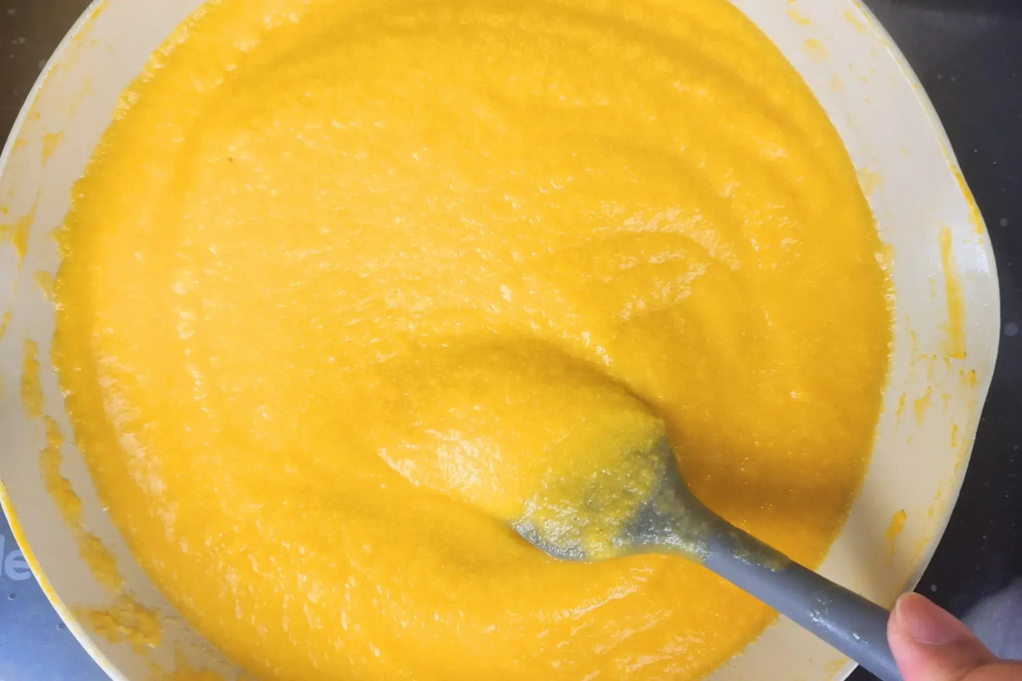 A hand is string pumpkin puree in a pan.