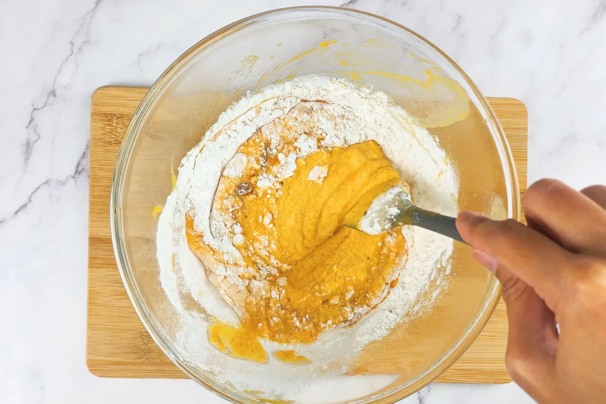 A hand is mixing pumpkin puree in a mixing bowl.