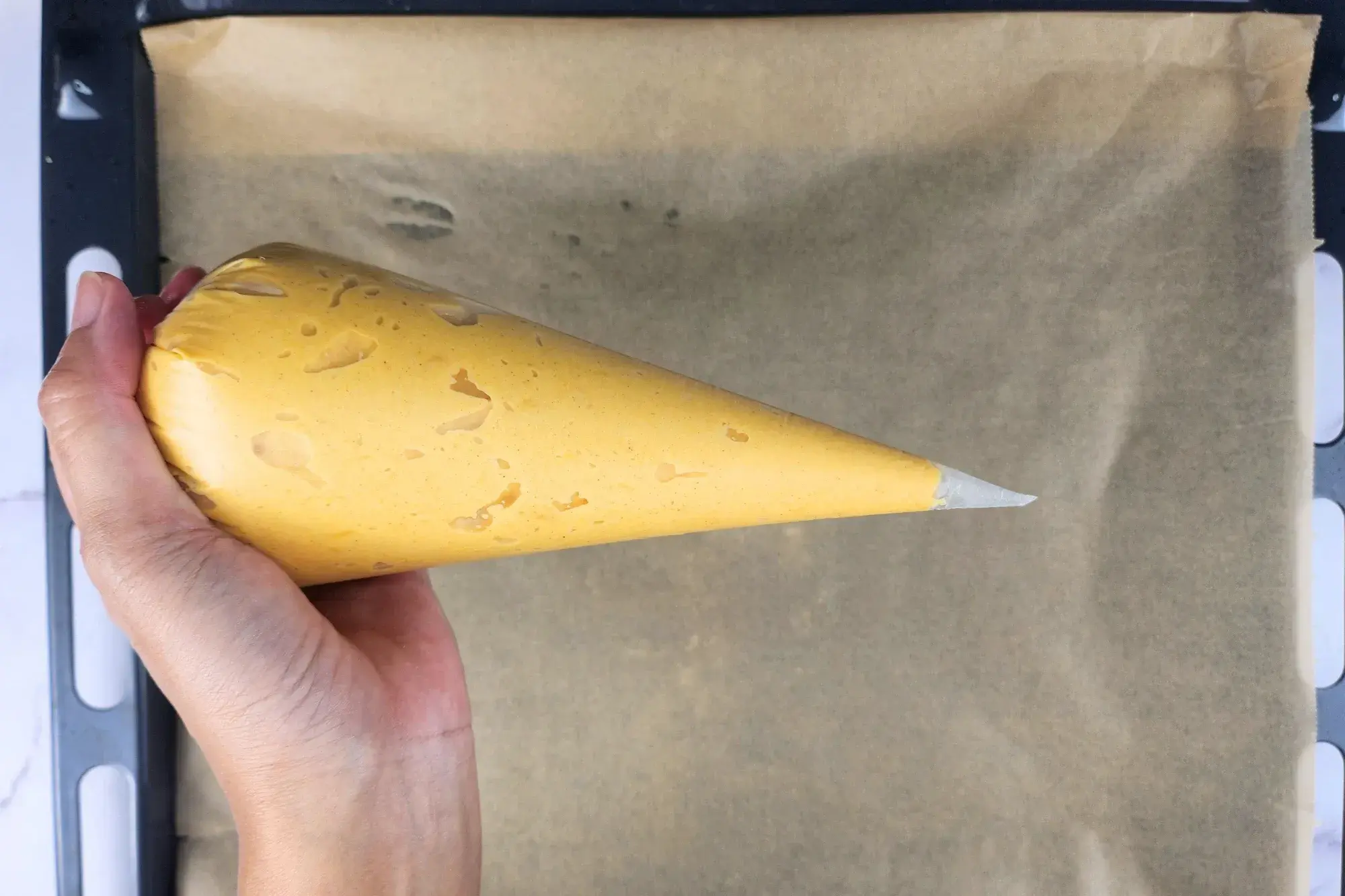 A hand is holding a piping bag above a baking paper.