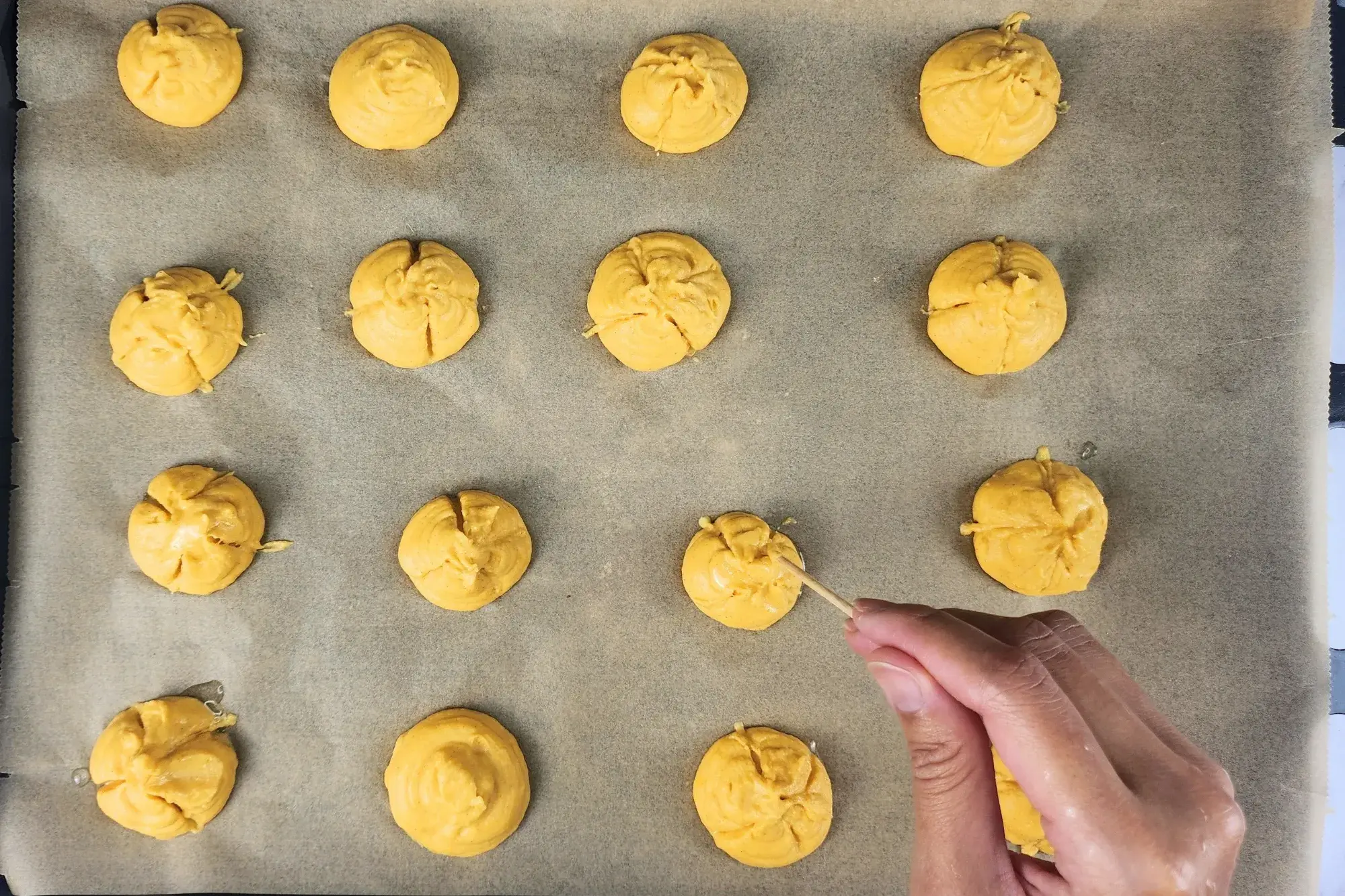 A hand is holding a screw above a pumpkin scoop on a baking paper