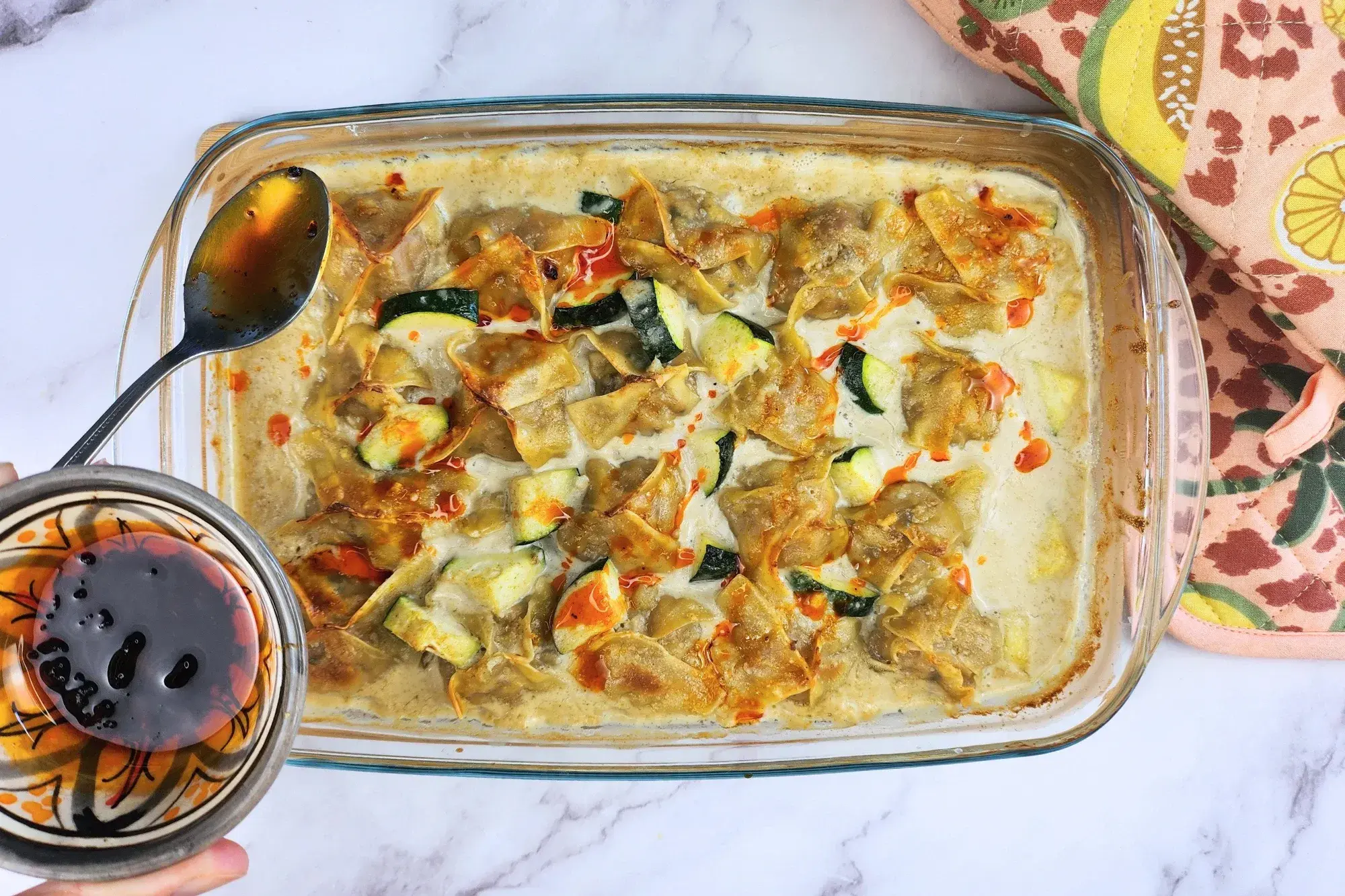 A bowl of chili oil and a spoon above a tray of food.