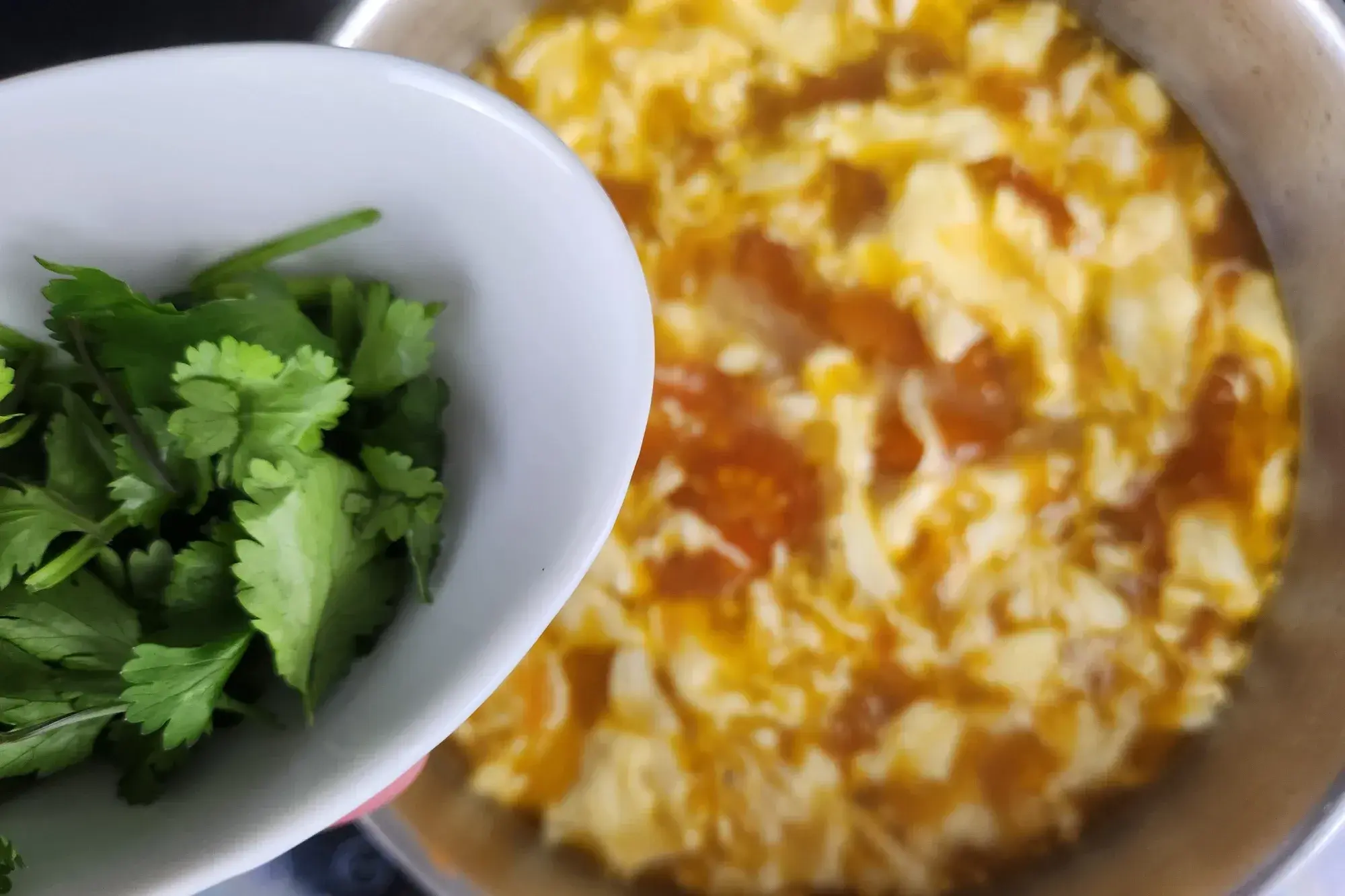 A bowl of chopped cilantro is above Tomato Egg Drop Soup.