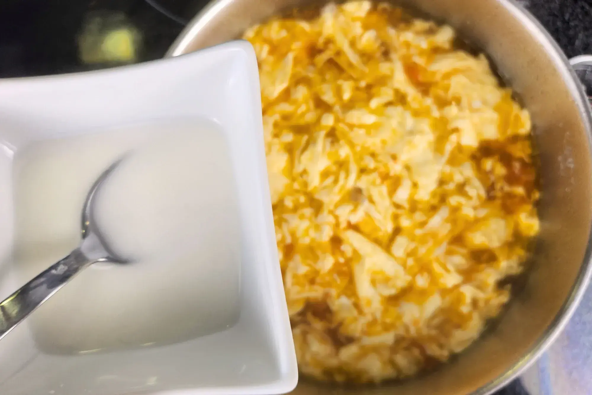 A bowl of cornstarch liquid is above of Tomato Egg Drop Soup .