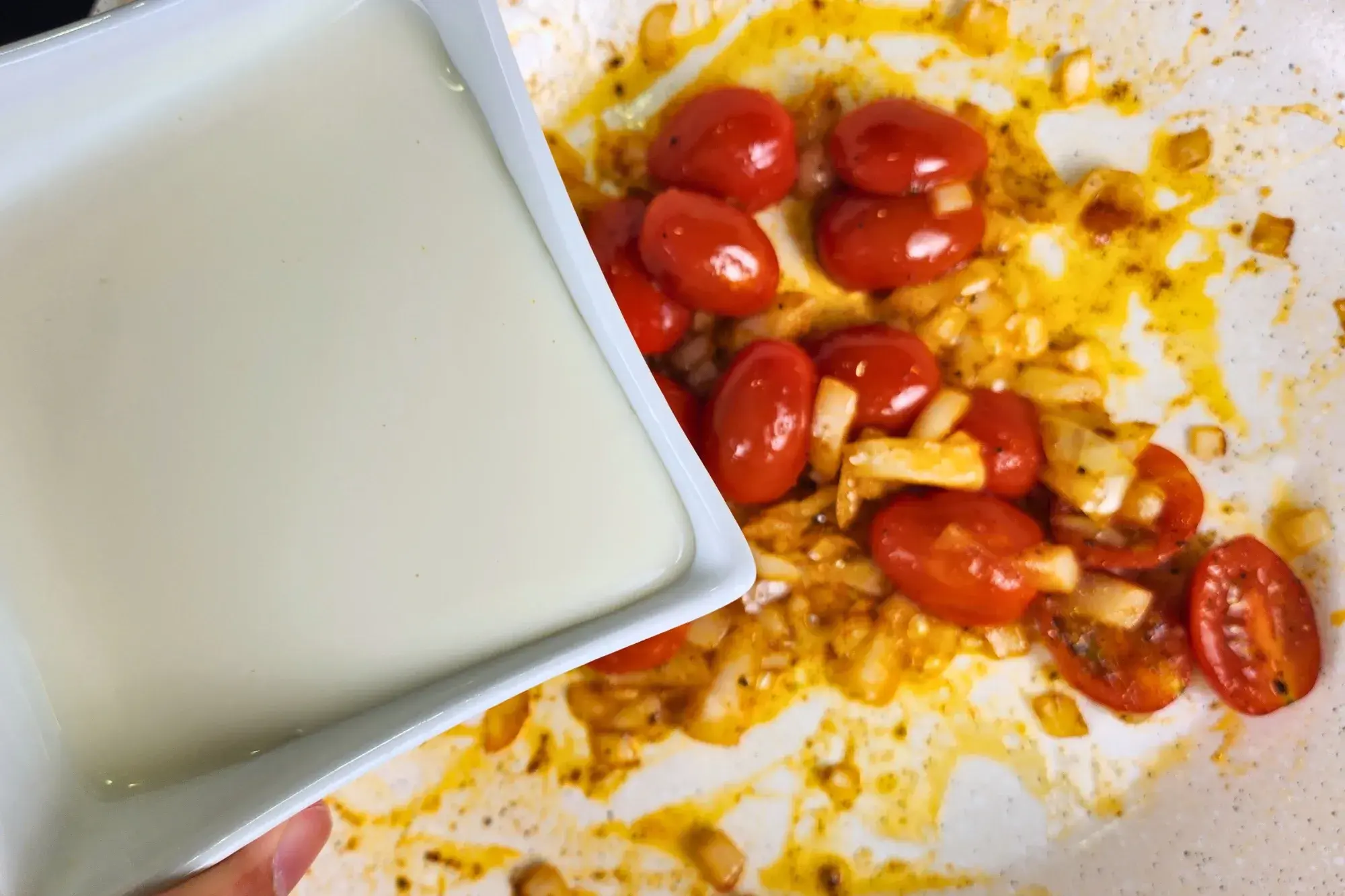 A bowl of cream sauce is above a pan