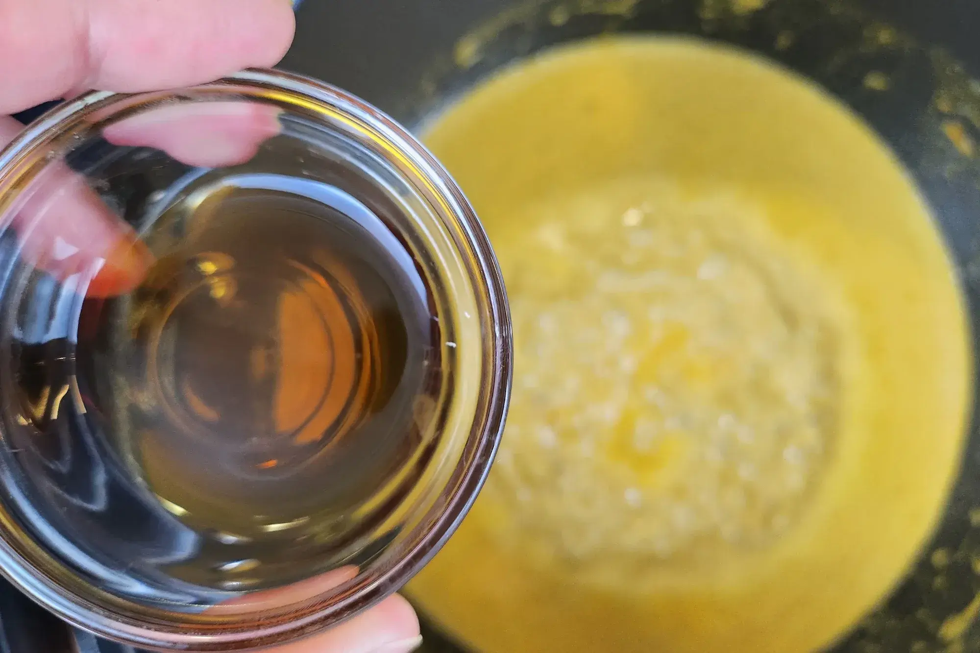 A bowl of fish sauce  is being holding above the curry pot.