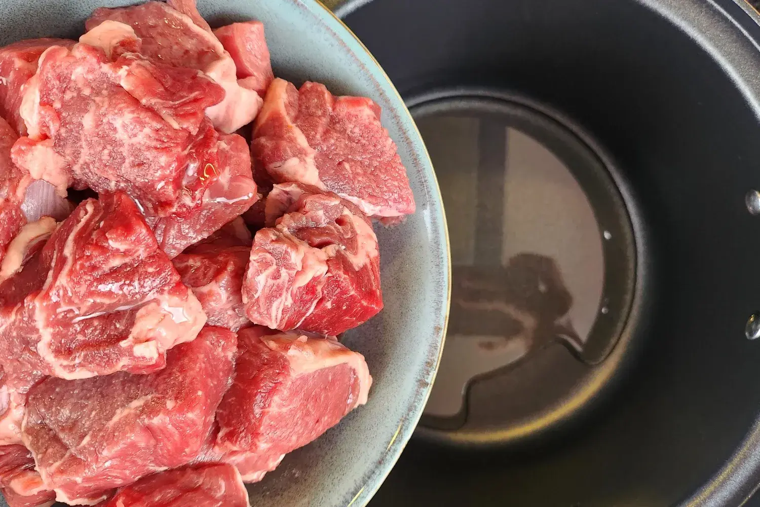 A bowl of meat above a pot