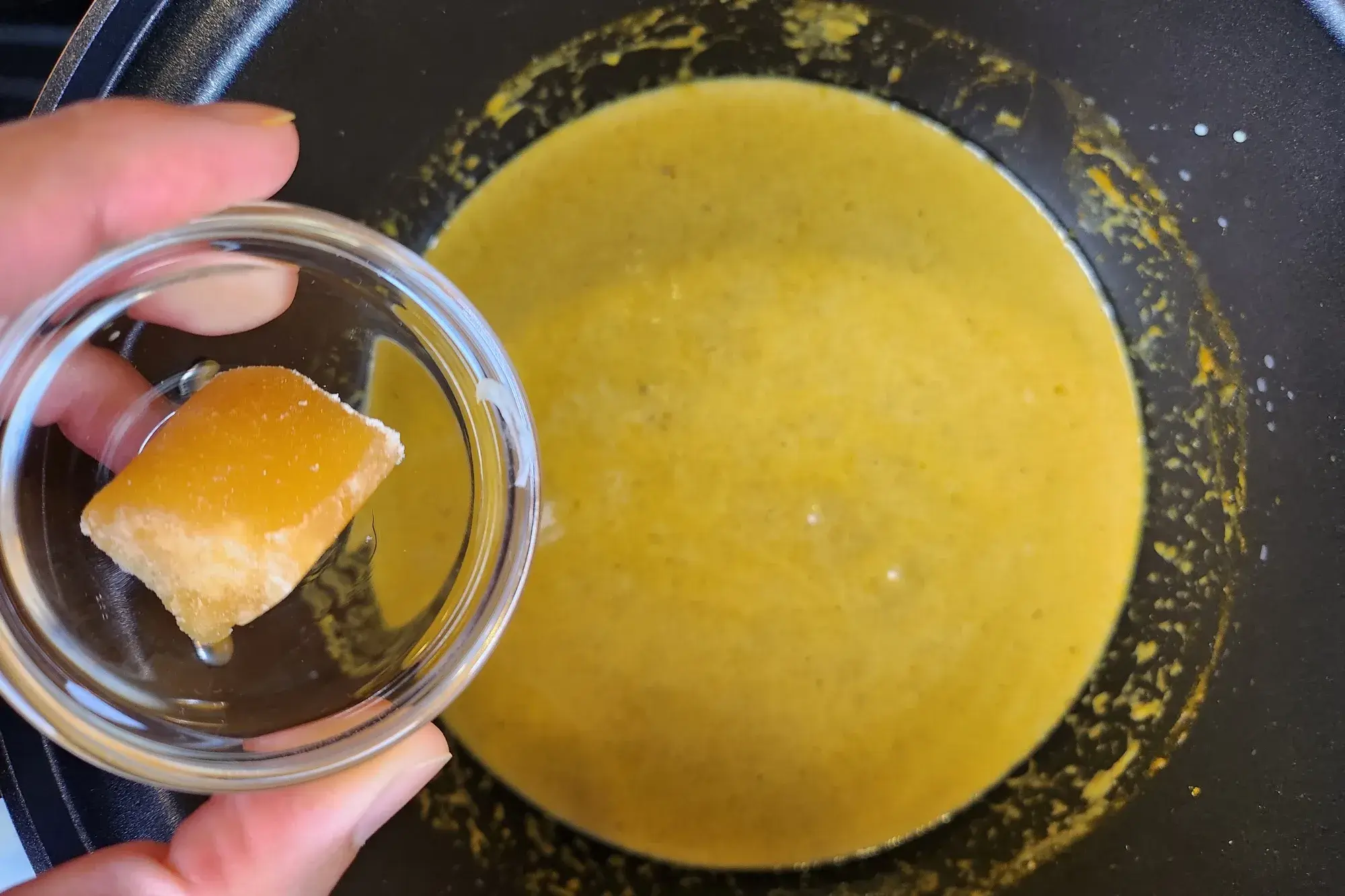 A bowl of palm sugar is being holding above the curry pot.