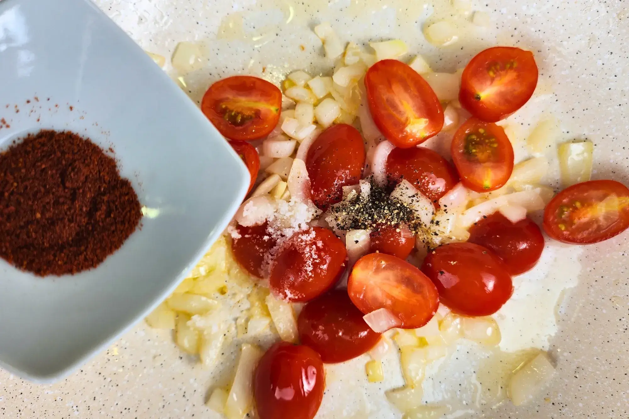 A bowl of paprika powder is above a pan