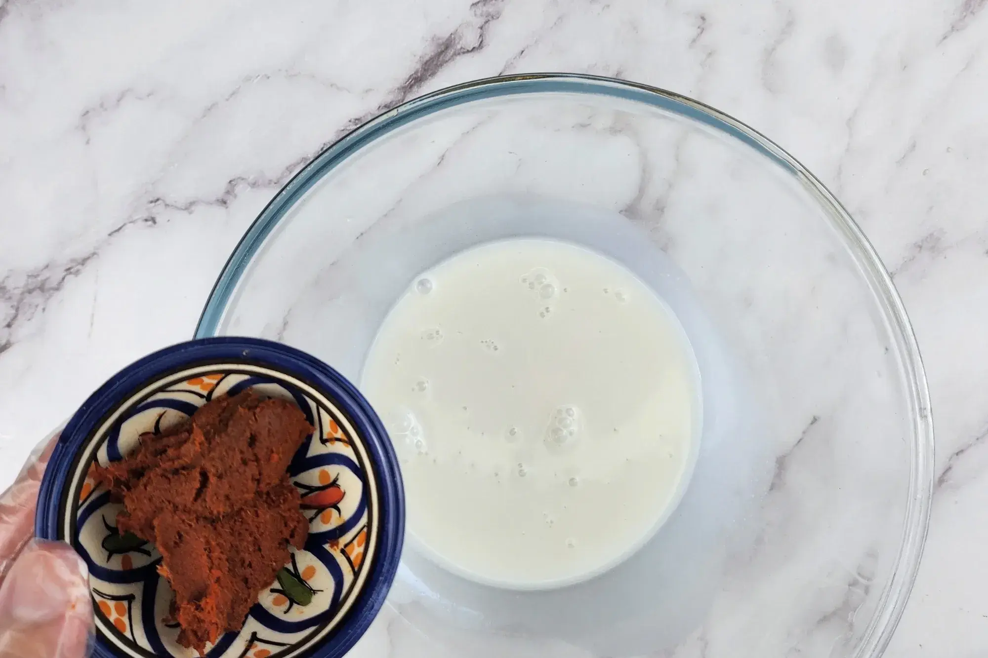 A bowl of red chili paste above of a mixing bowl of coconut milk