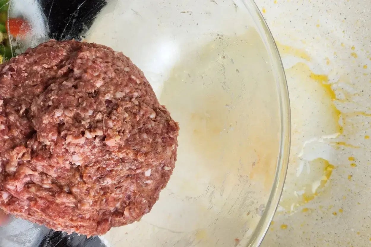 A bowl of seasoned ground beef above an used wok.