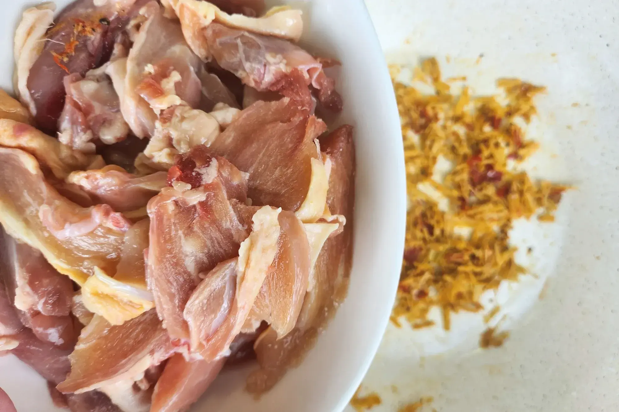 A bowl of sliced chicken is above a wok with cooked lemongrass chili paste.