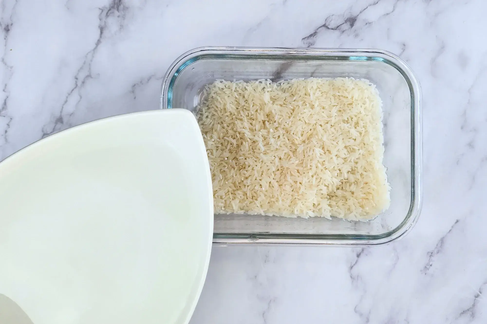 A bowl of water above uncooked jasmine rice.
