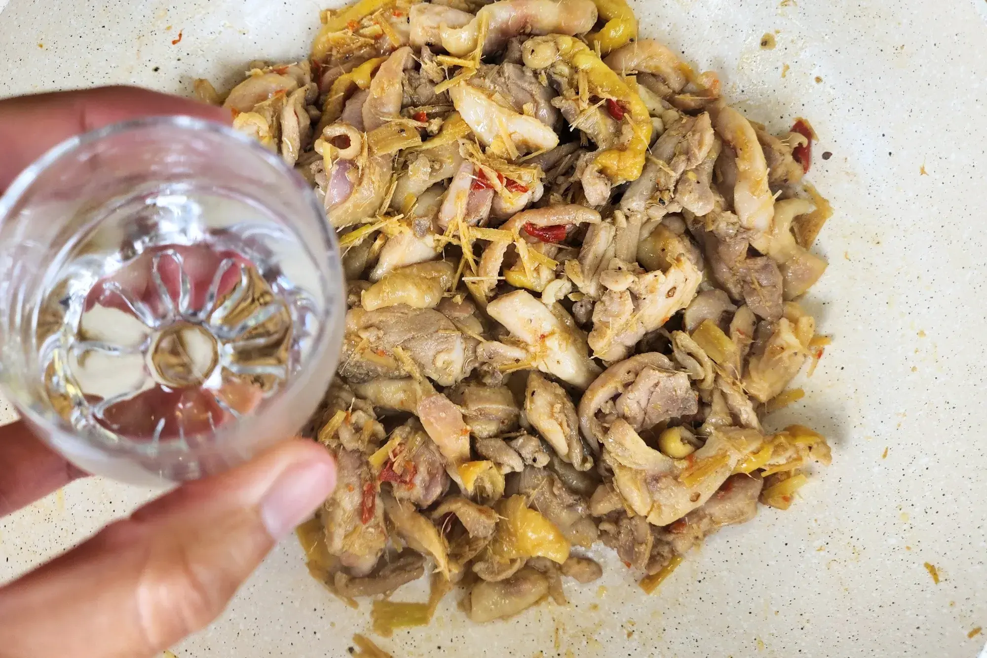A bowl of water in above cooked chicken in a wok.