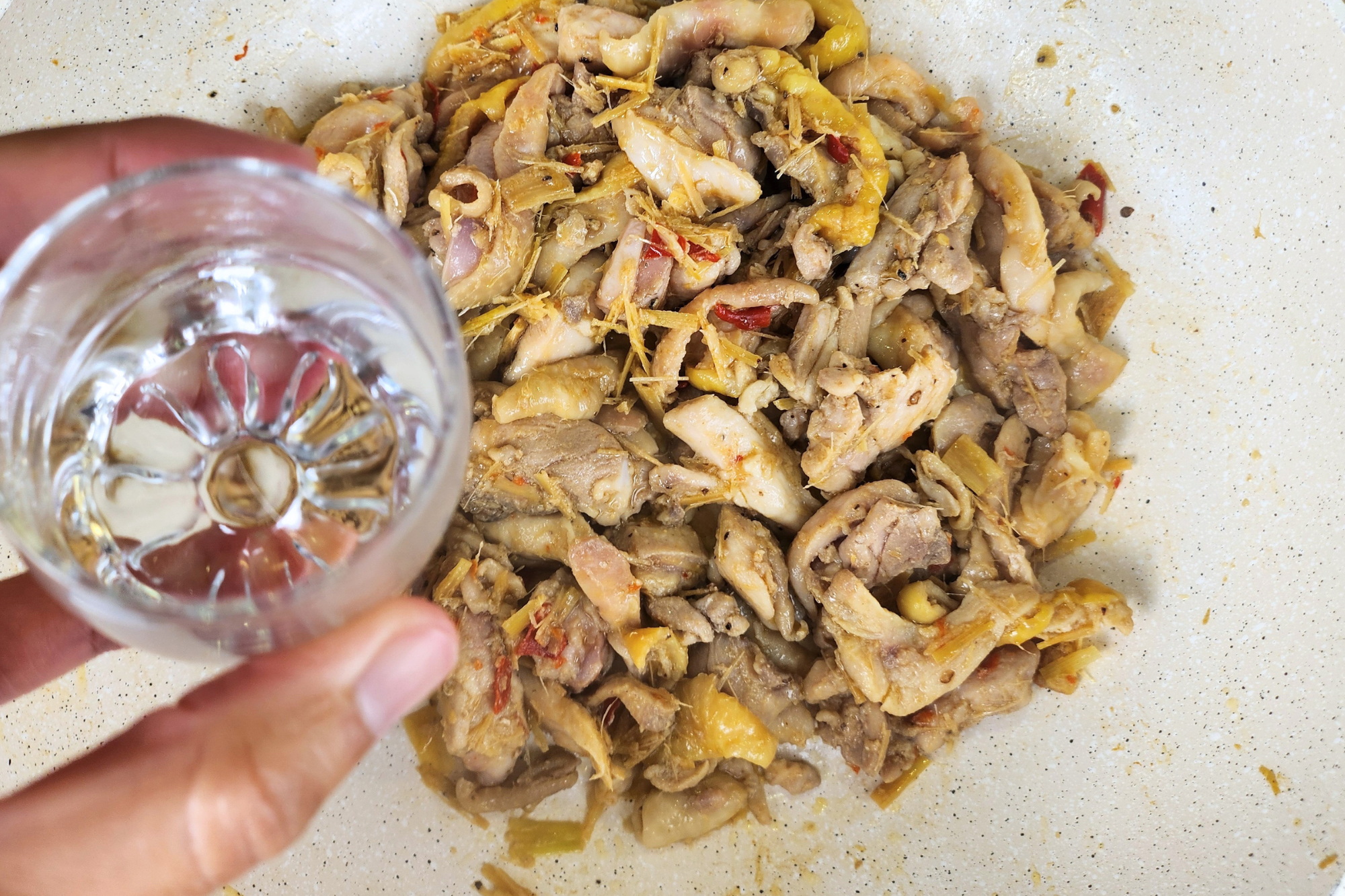 A bowl of water in above cooked chicken in a wok.