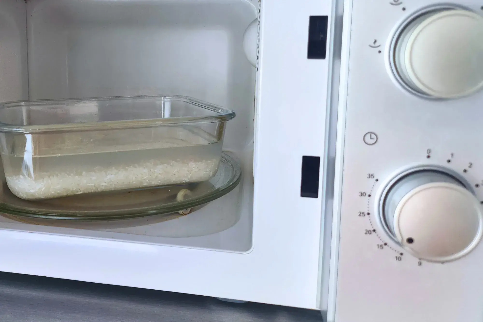 A container with jasmine rice with water inside a microwave.