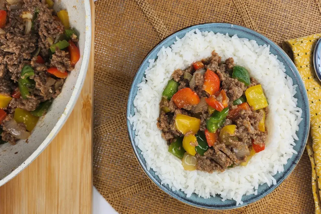 A ground beef and bell pepper in a rice bowl and in a wok.
