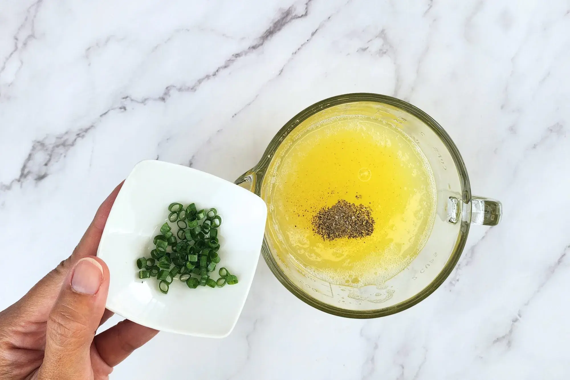 A hand holding a bowl of chopped green onions above the egg white