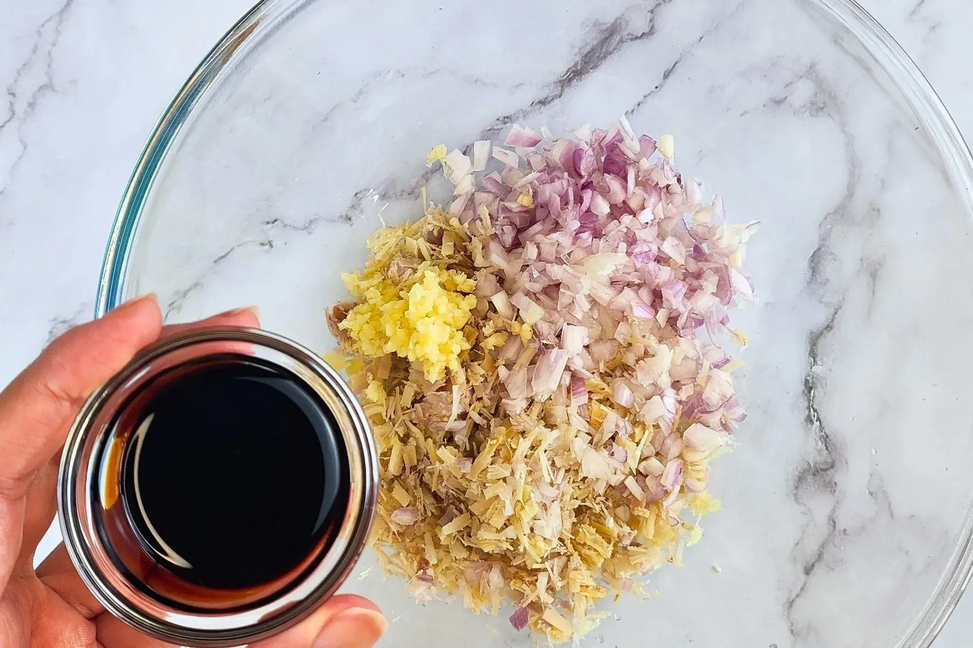 A hand holding a bowl of minced garlic above a mixing bowl