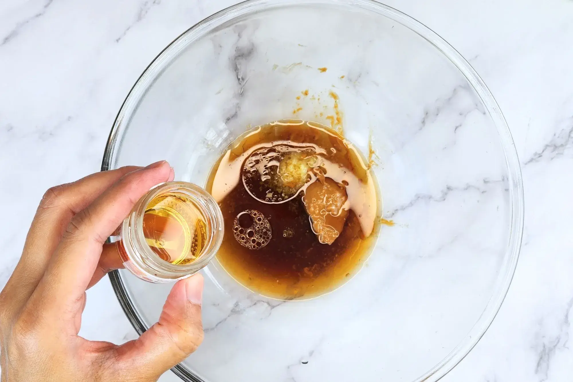 A hand holding a bowl of honey above the dressing bowl