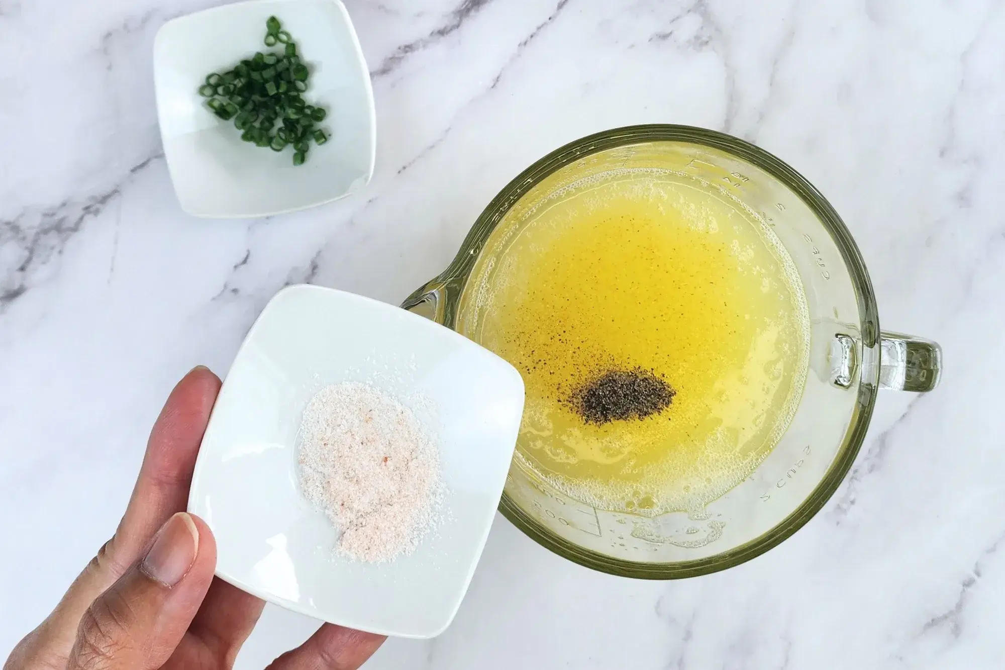 A hand holding a bowl of salt above the egg white and anpther ingredient