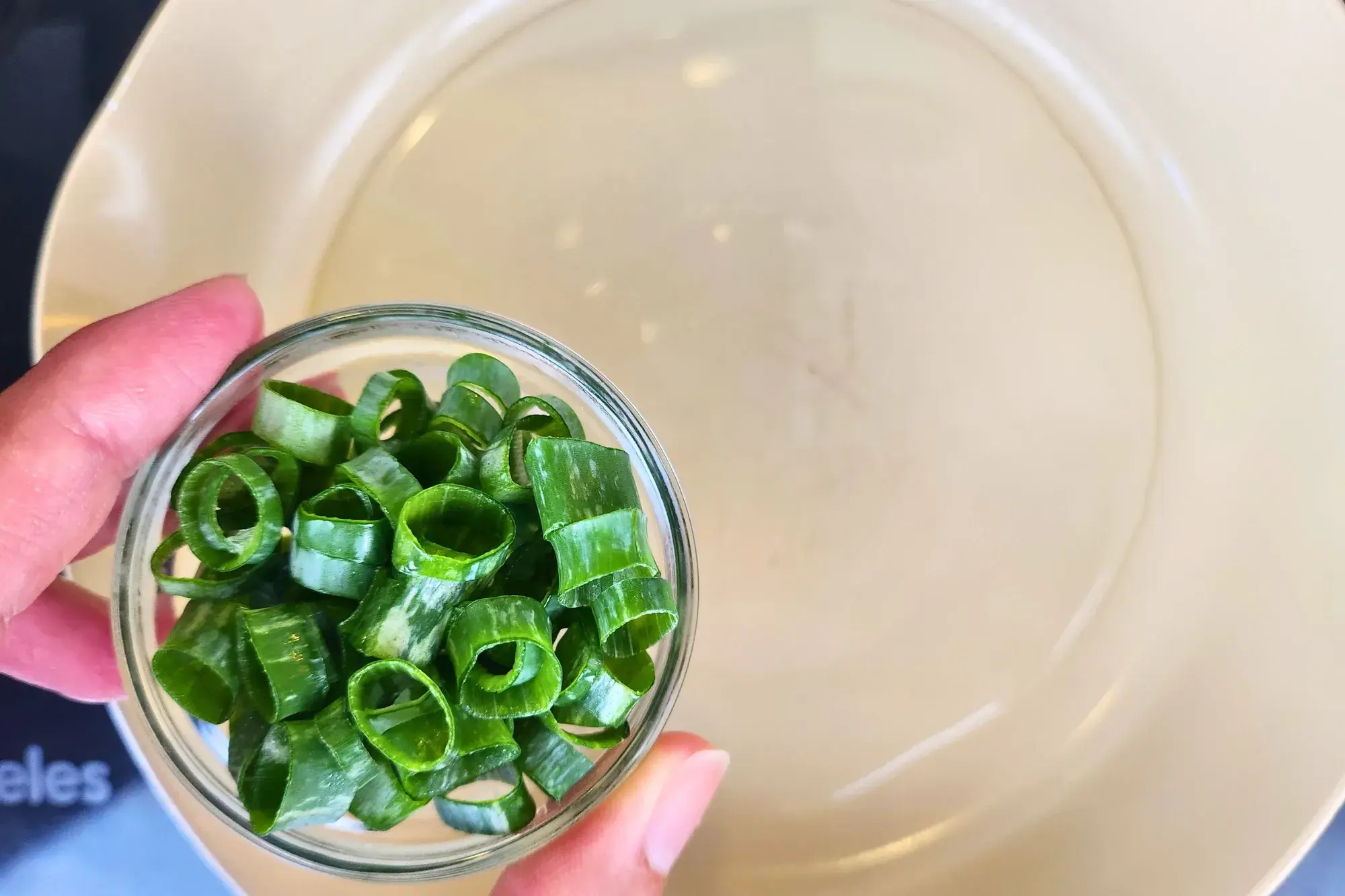 A hand holding a bowl of scallions above a pan