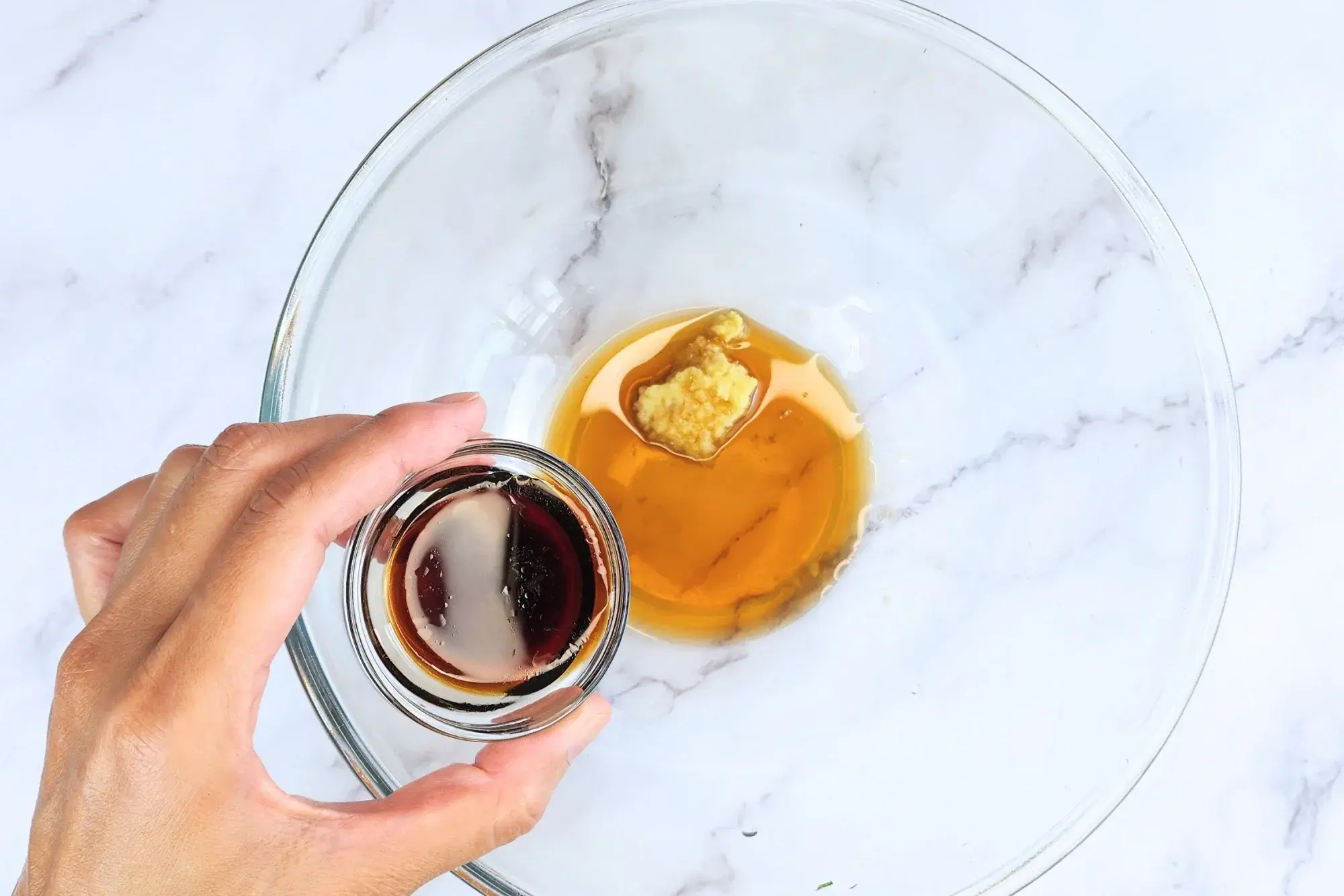 A hand holding a bowl of soy sauce above the dressing bowl