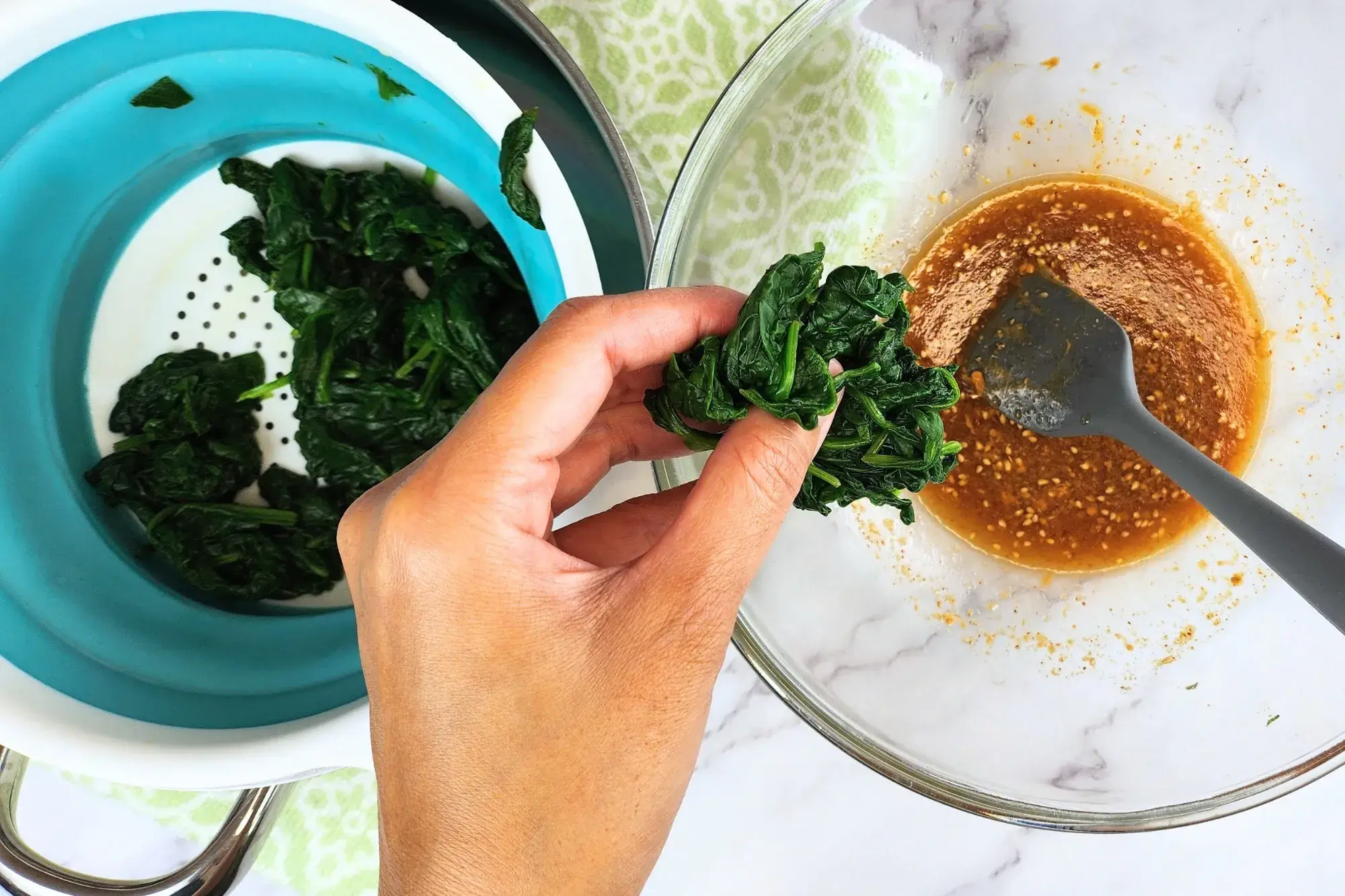 A hand holding a bunch of spinach above the dressing bowl