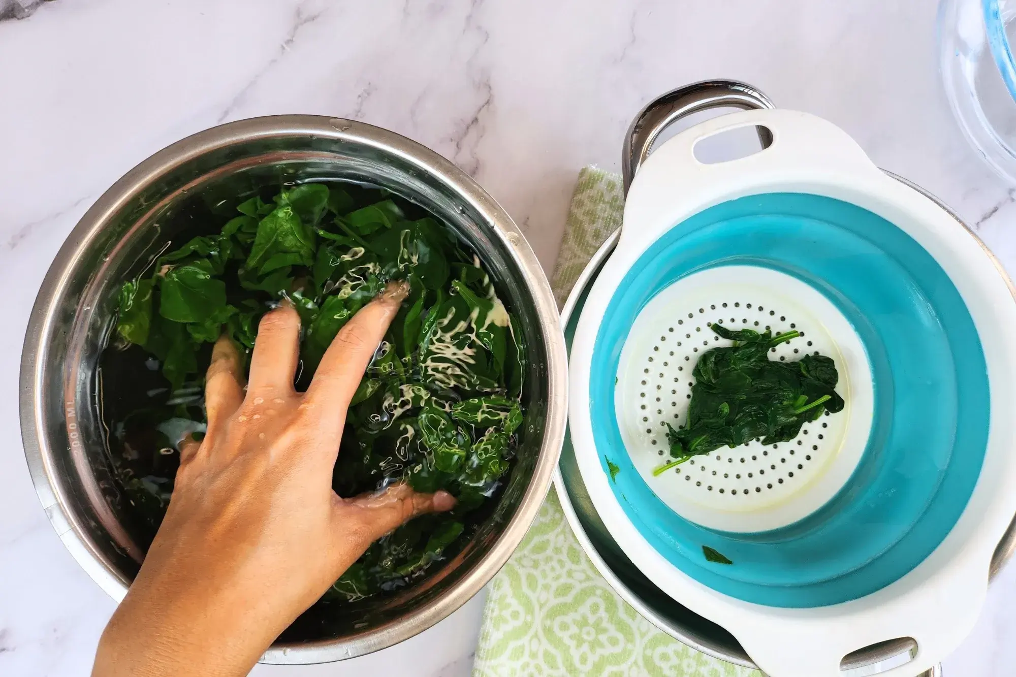 A hand is grabbing spinach in water bowl
