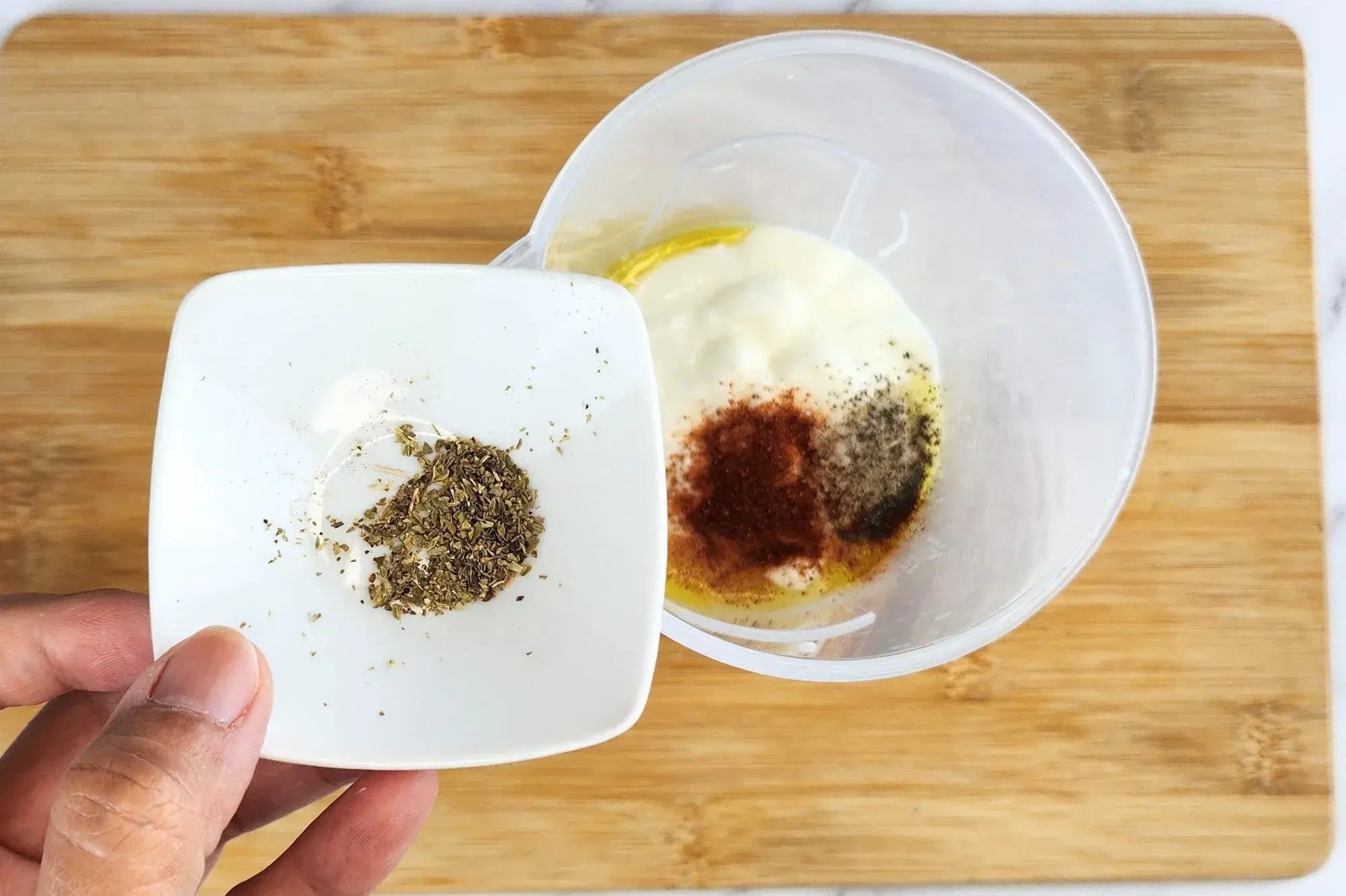 A hand is hold a bowl of origano above a jar of cooked center of zucchini