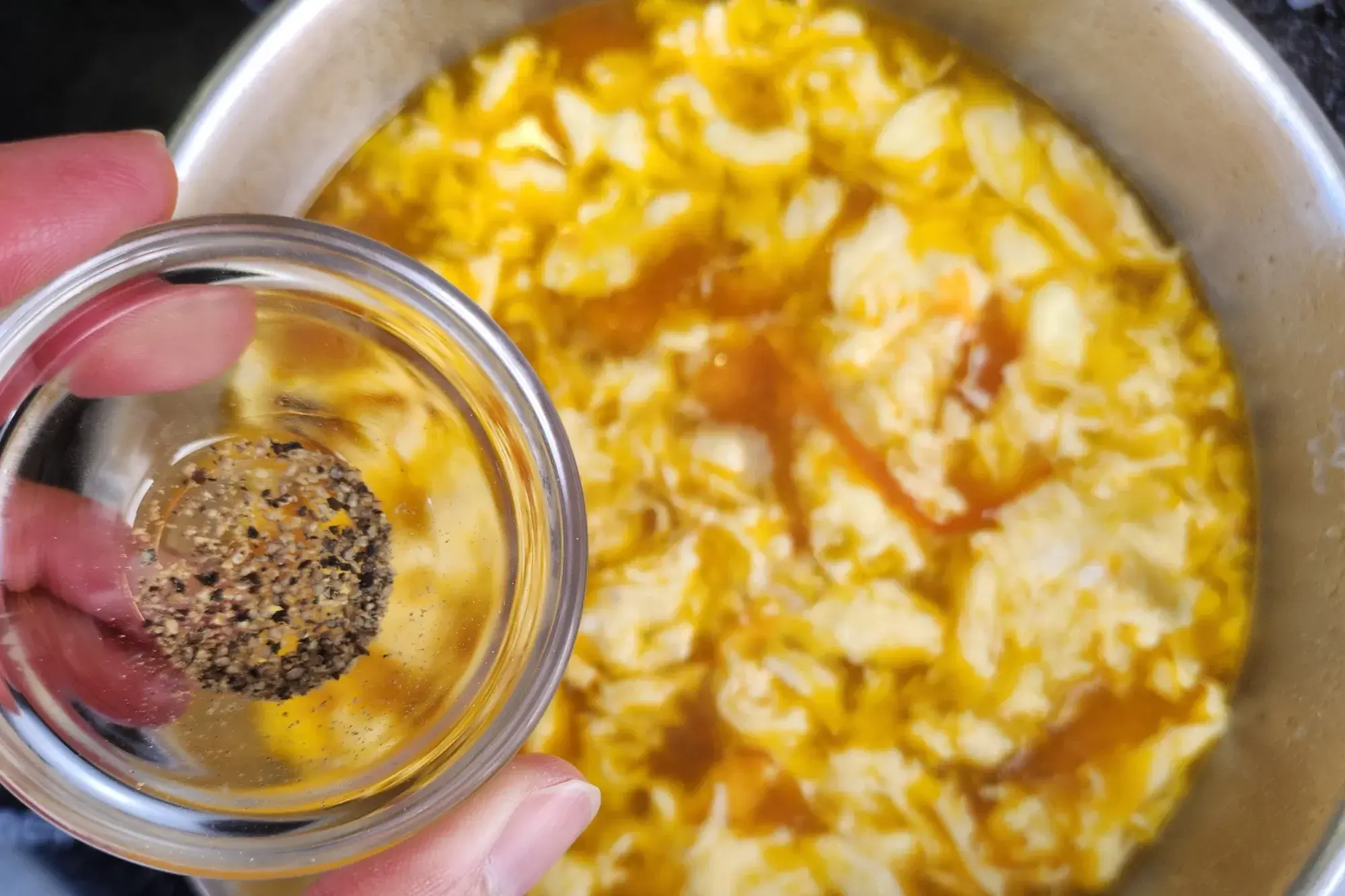 A hand is hold a bowl of pepper powder is above of Tomato Egg Drop Soup.