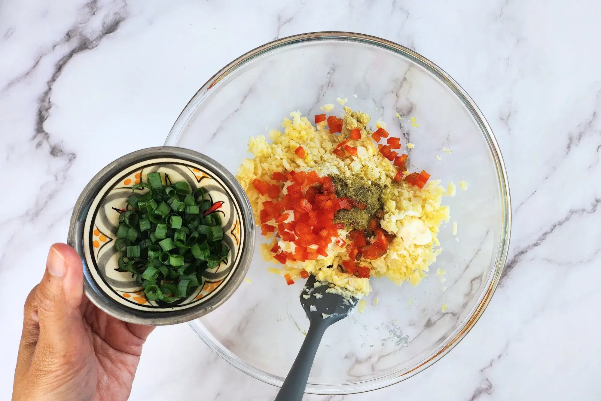 A hand is holding a bowl of chopped green onion above the mixing bowl.