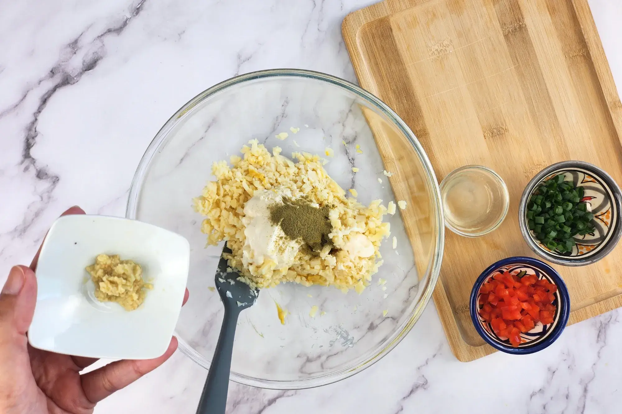 A hand is holding a bowl of grated ginger above the mixing bowl.