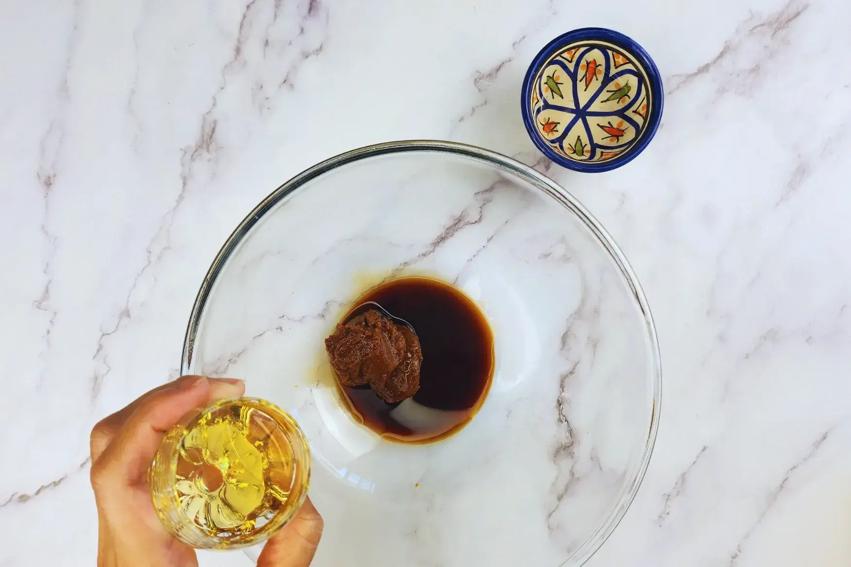 A hand is holding a bowl of honey above a mixing bowl.
