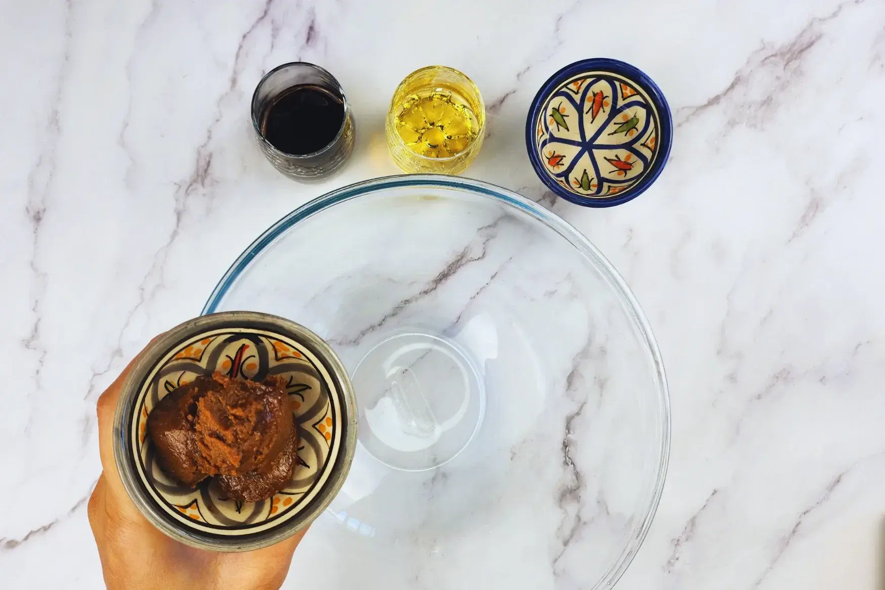 A hand is holding a bowl of miso paste above the mixing bowl.