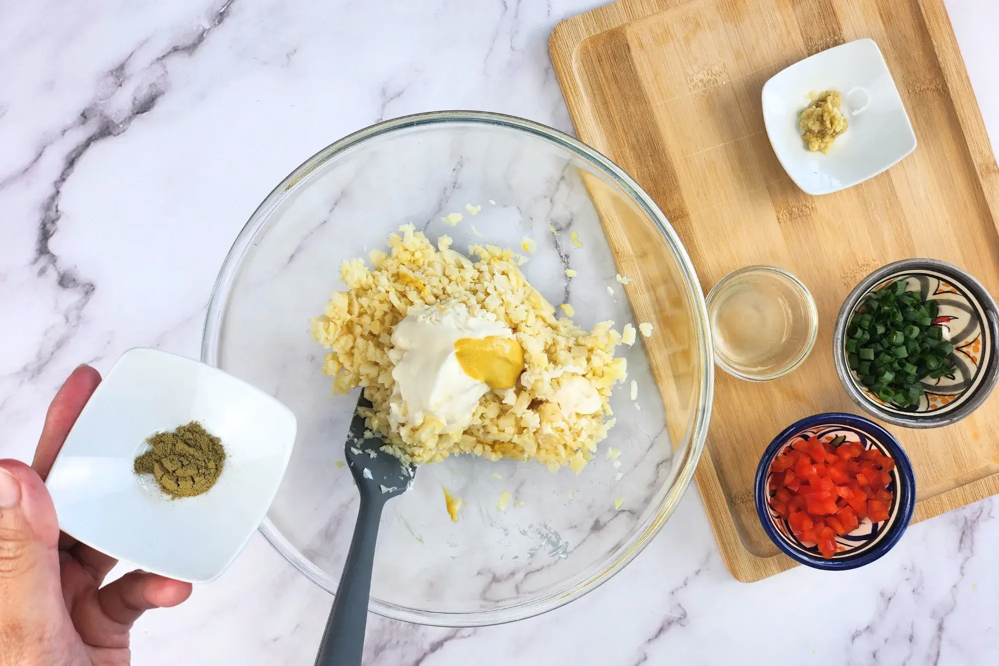 A hand is holding a bowl of old bay seasoning above the mixing bowl.