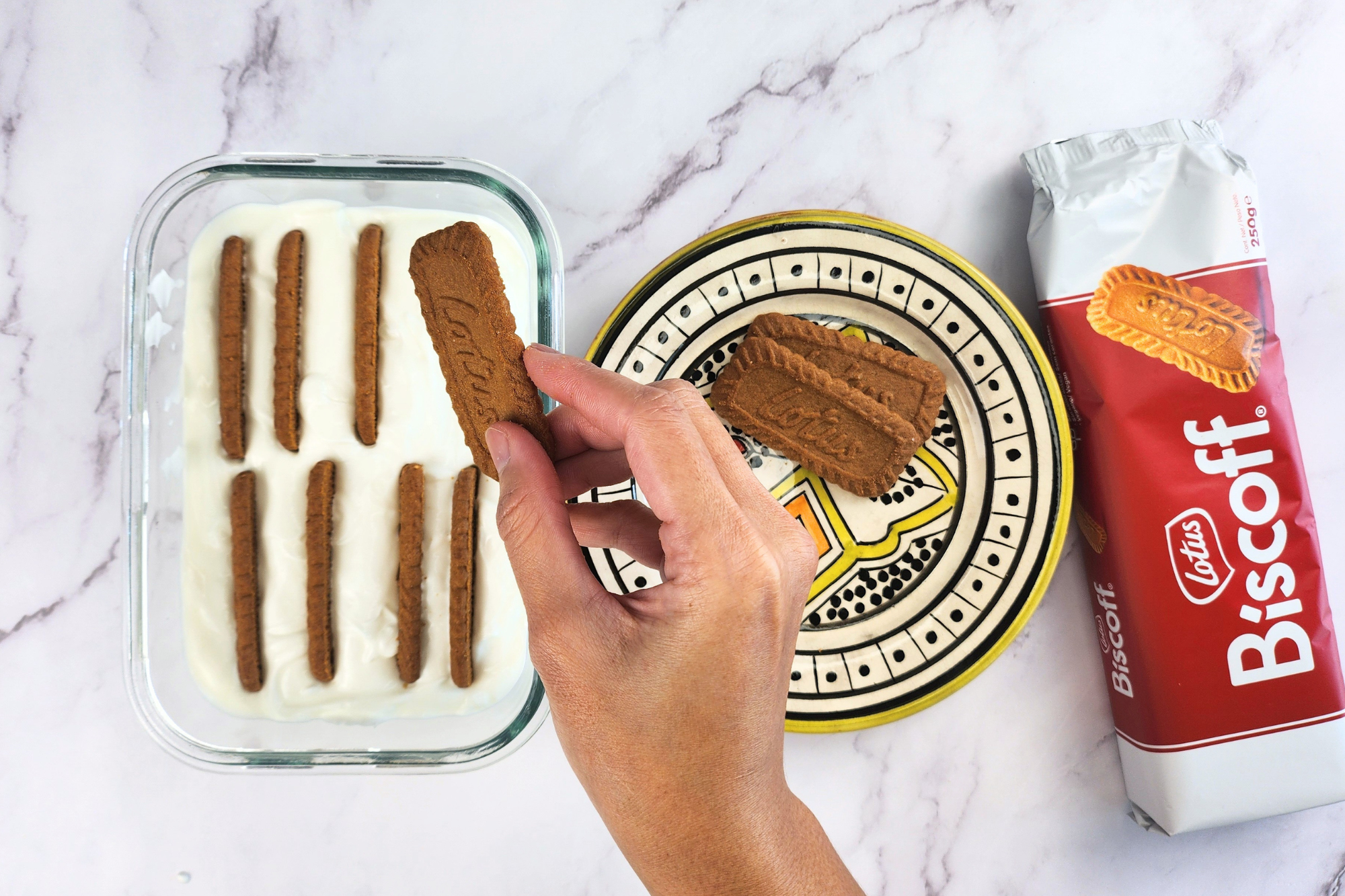 A hand is holding a cookie above a bowl of yogurt.