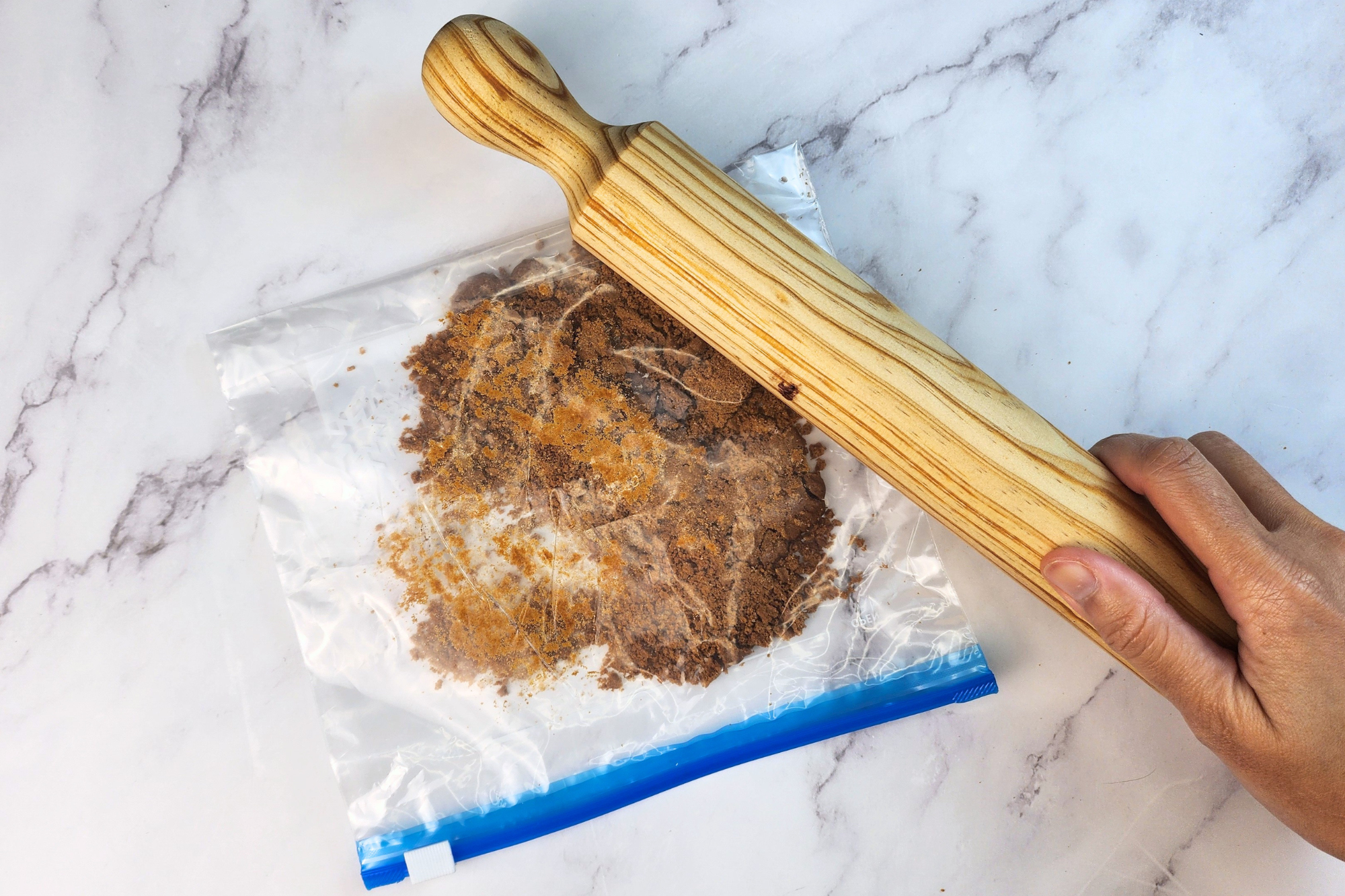 A hand is holding a pin is on a bag of cookie crumbles.