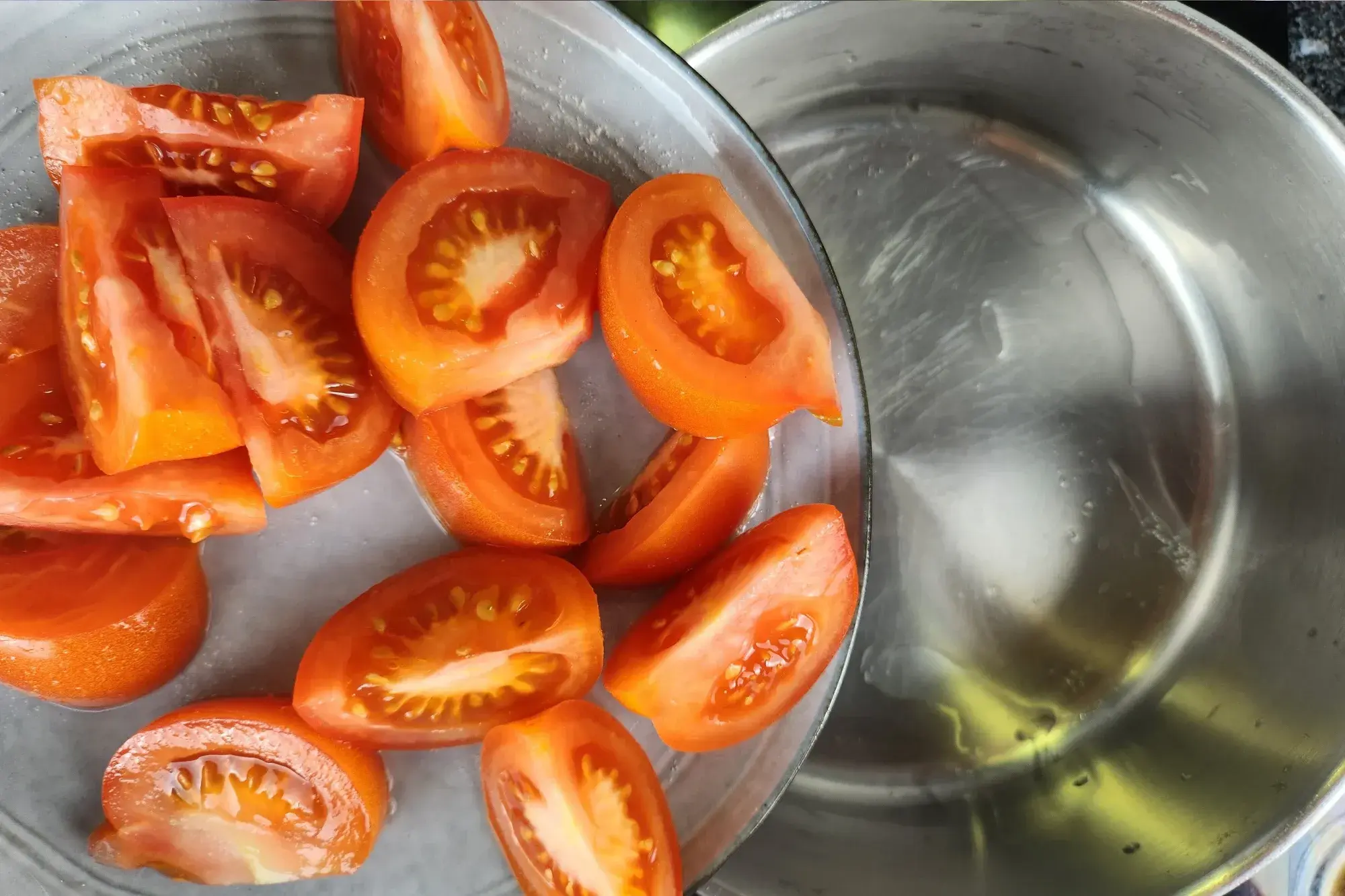 A hand is holding a plate of tomato wedges above a pot.