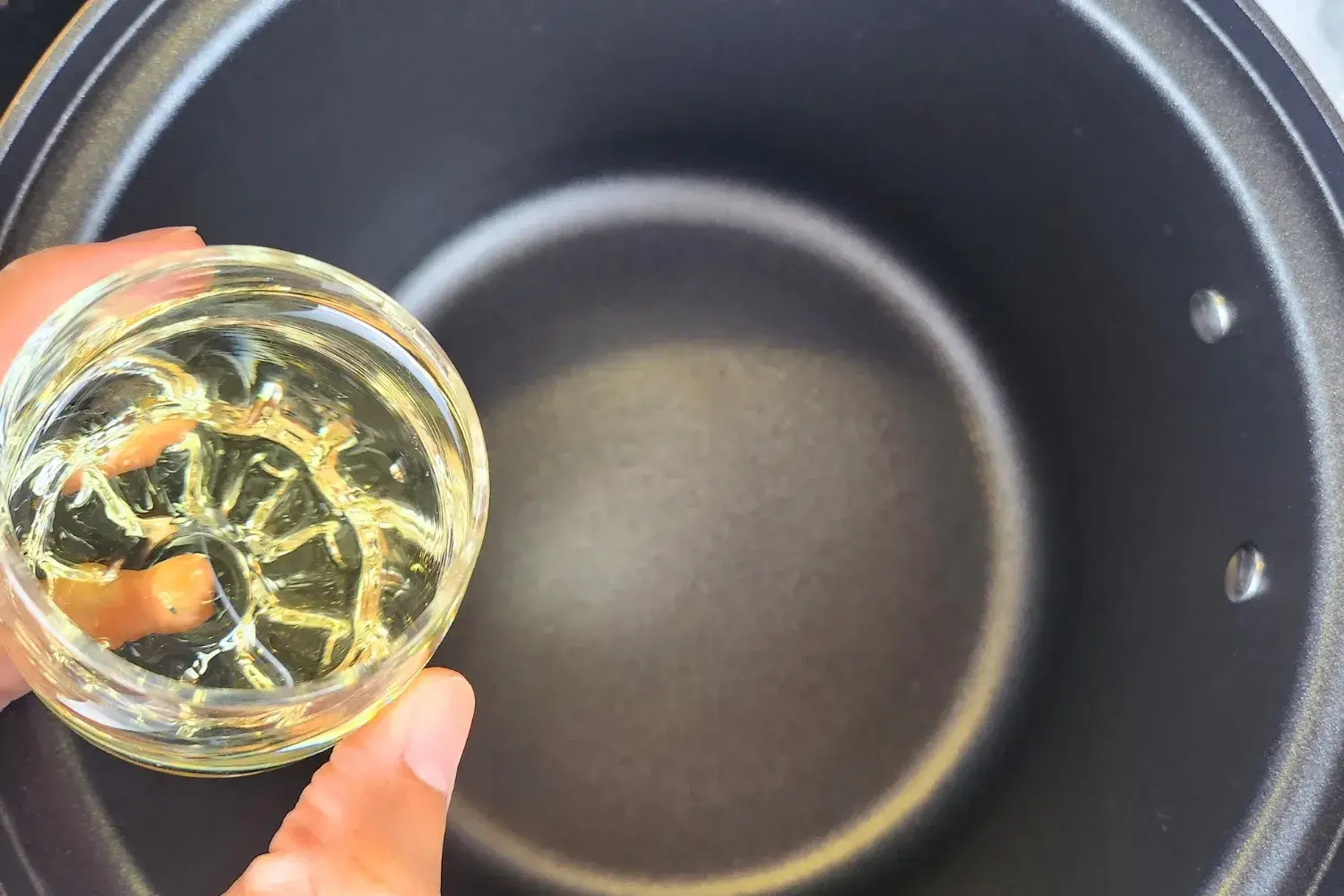 A hand is holding a small bowl of cooking oil.