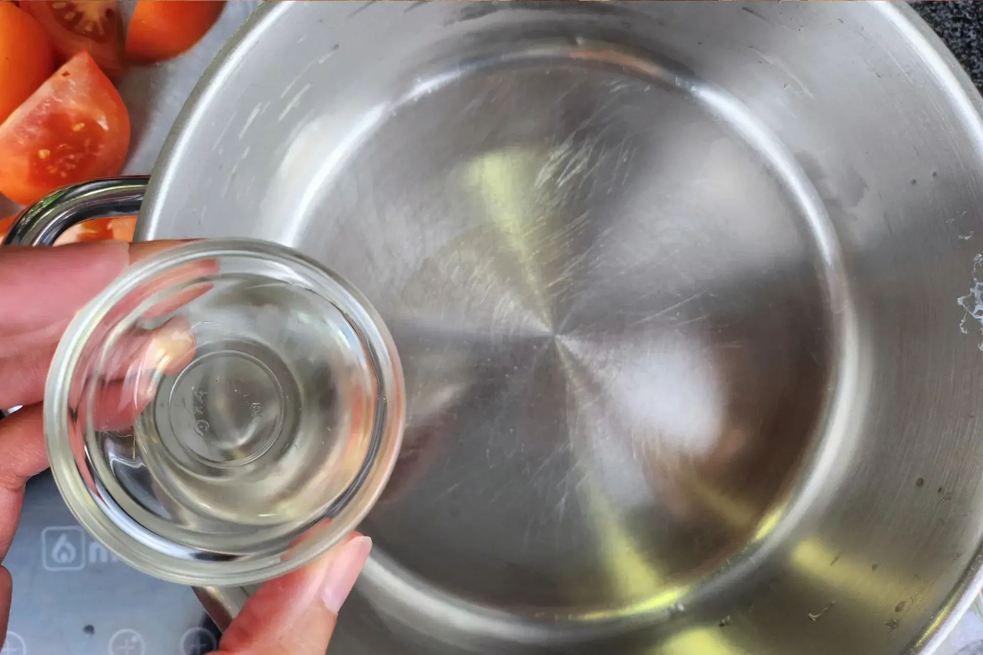 A hand is holding a small bowl of oil above a pot.