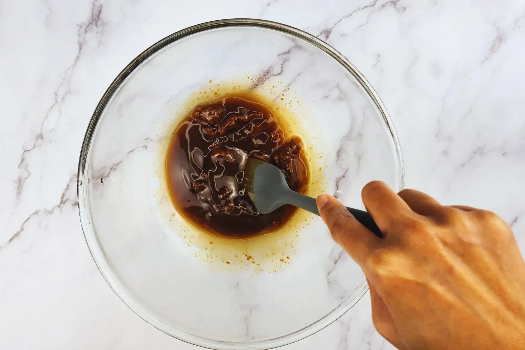 A hand is holding a spatula mixed miso sauce in a mixing bowl.