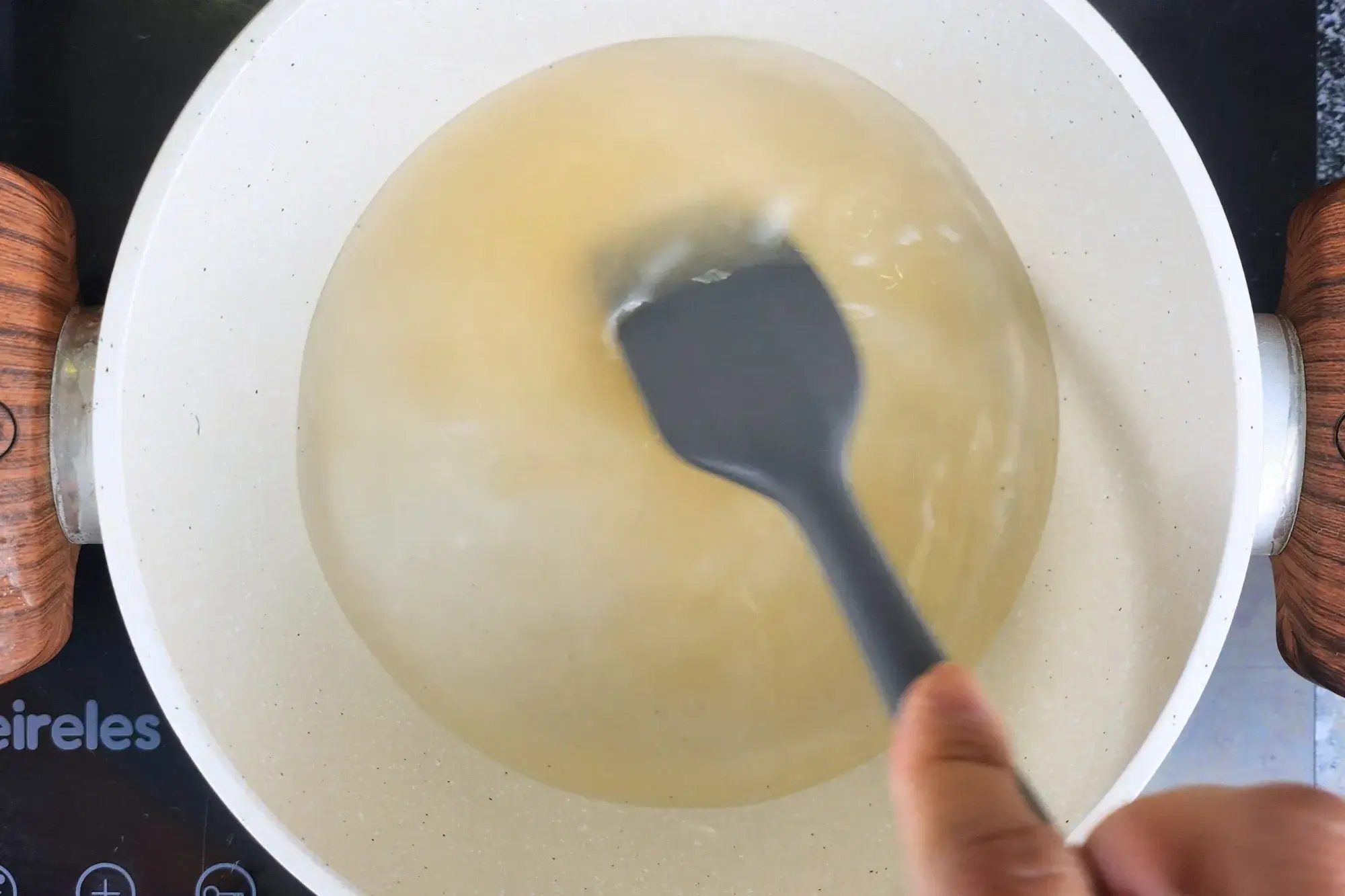 A hand is holding a spatula stir the pot of water