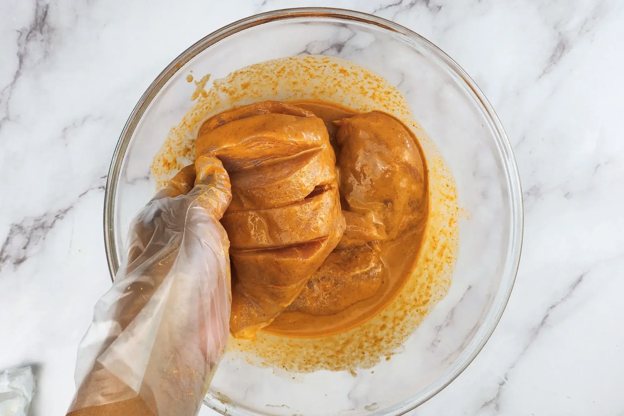 A hand is holding chicken breast covered with marinating sauce