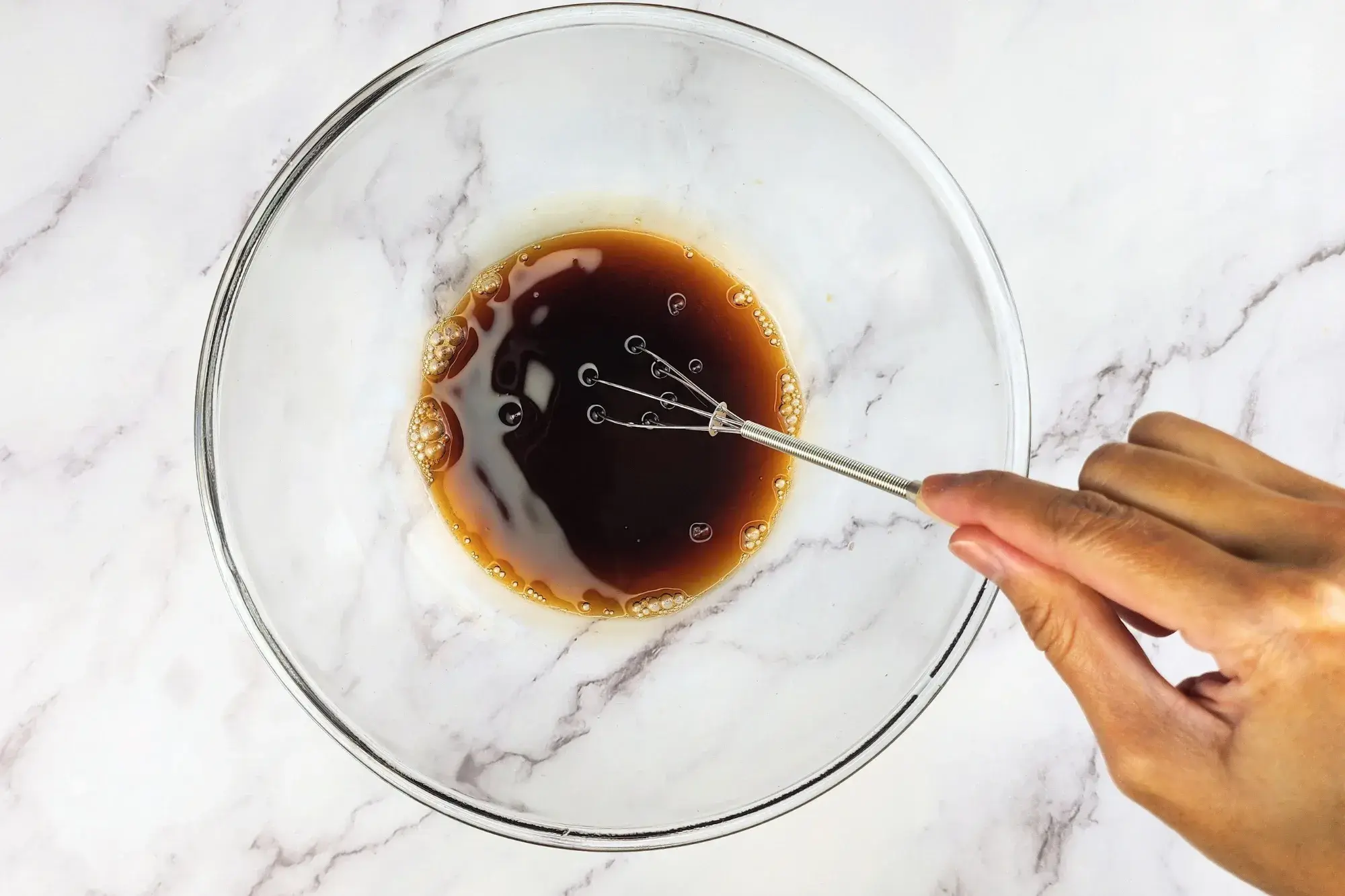 A hand is mixing sauce in a glass bowl.