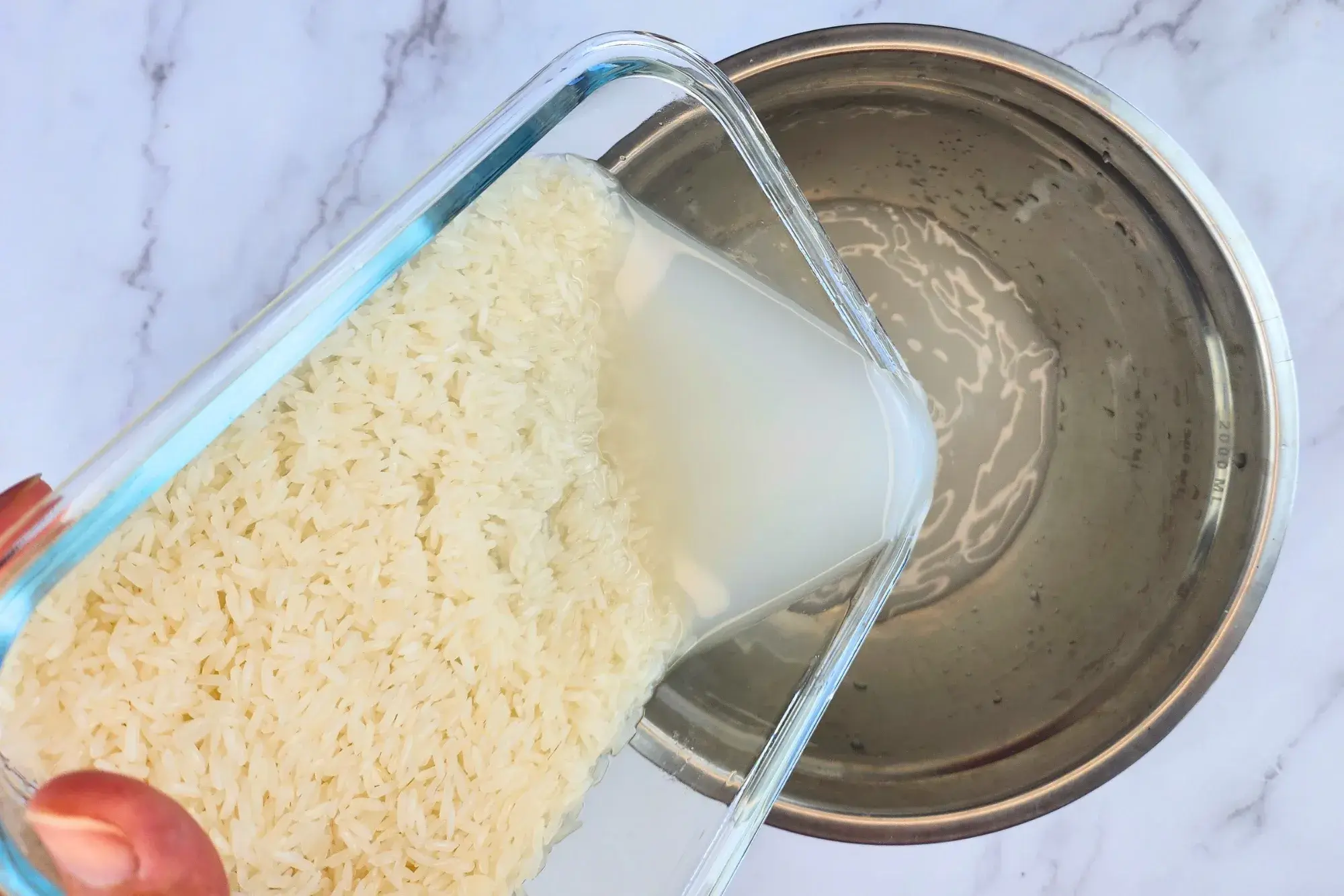 A hand rinse water out of a container of jasmine rice