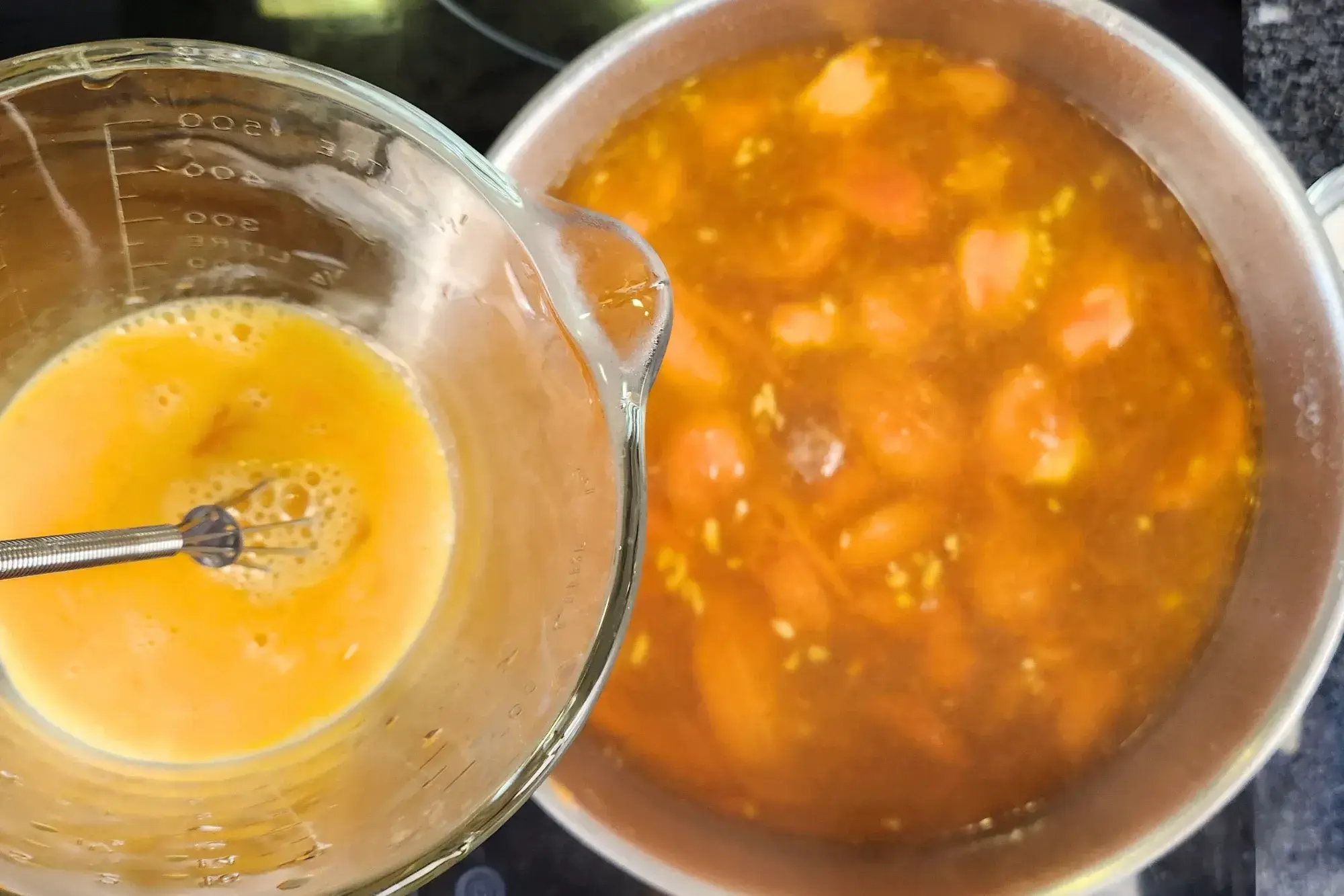 A jar of beaten egg is above tomato soup.