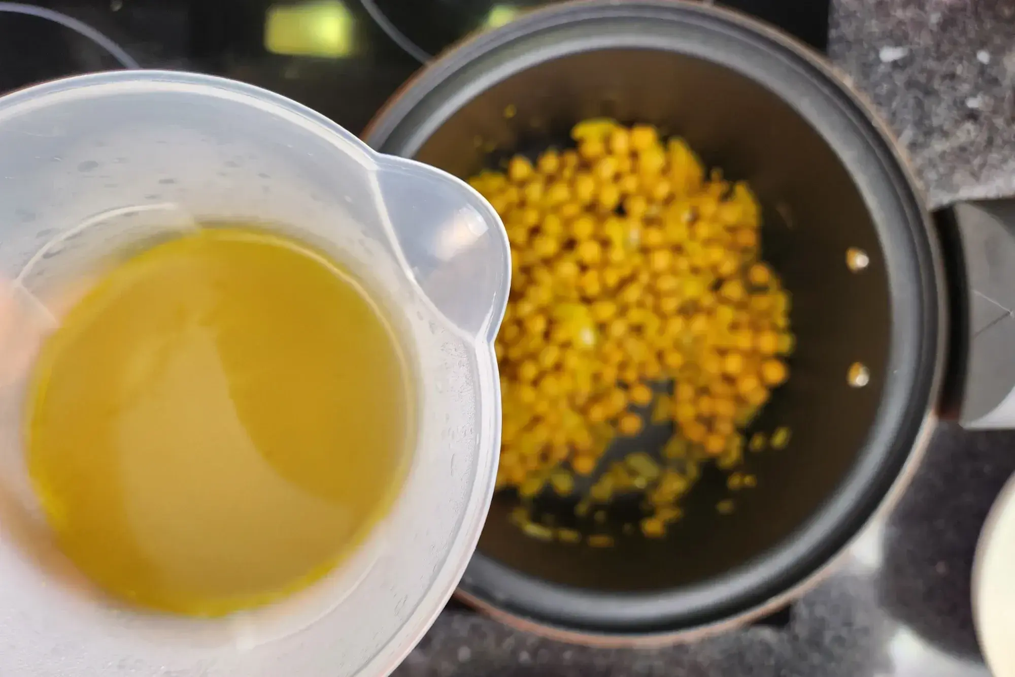 A jar of broth above a pot with cooked chicpeas