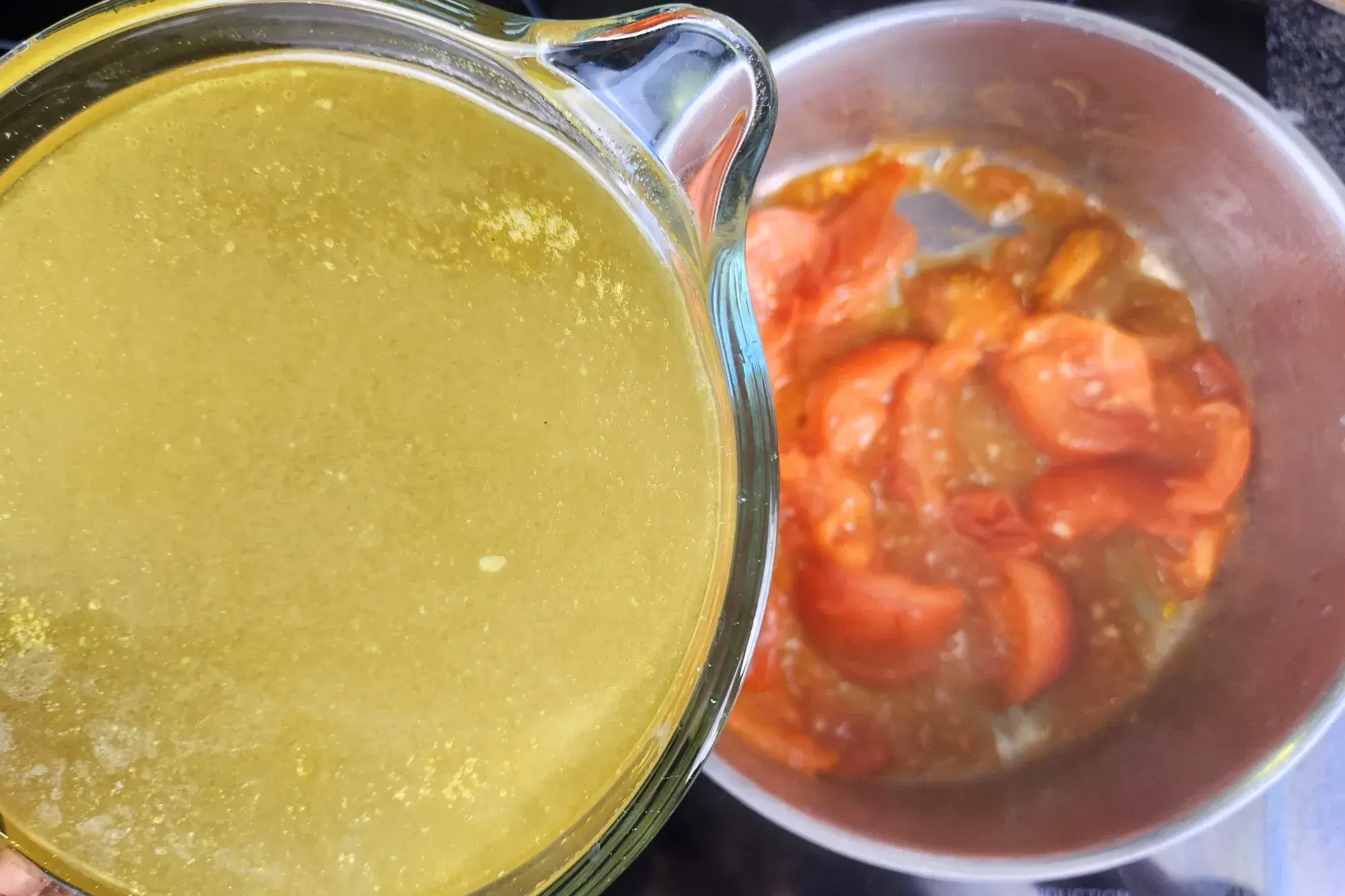 A jar of chicken stock is above a cooked tomatoes pot.