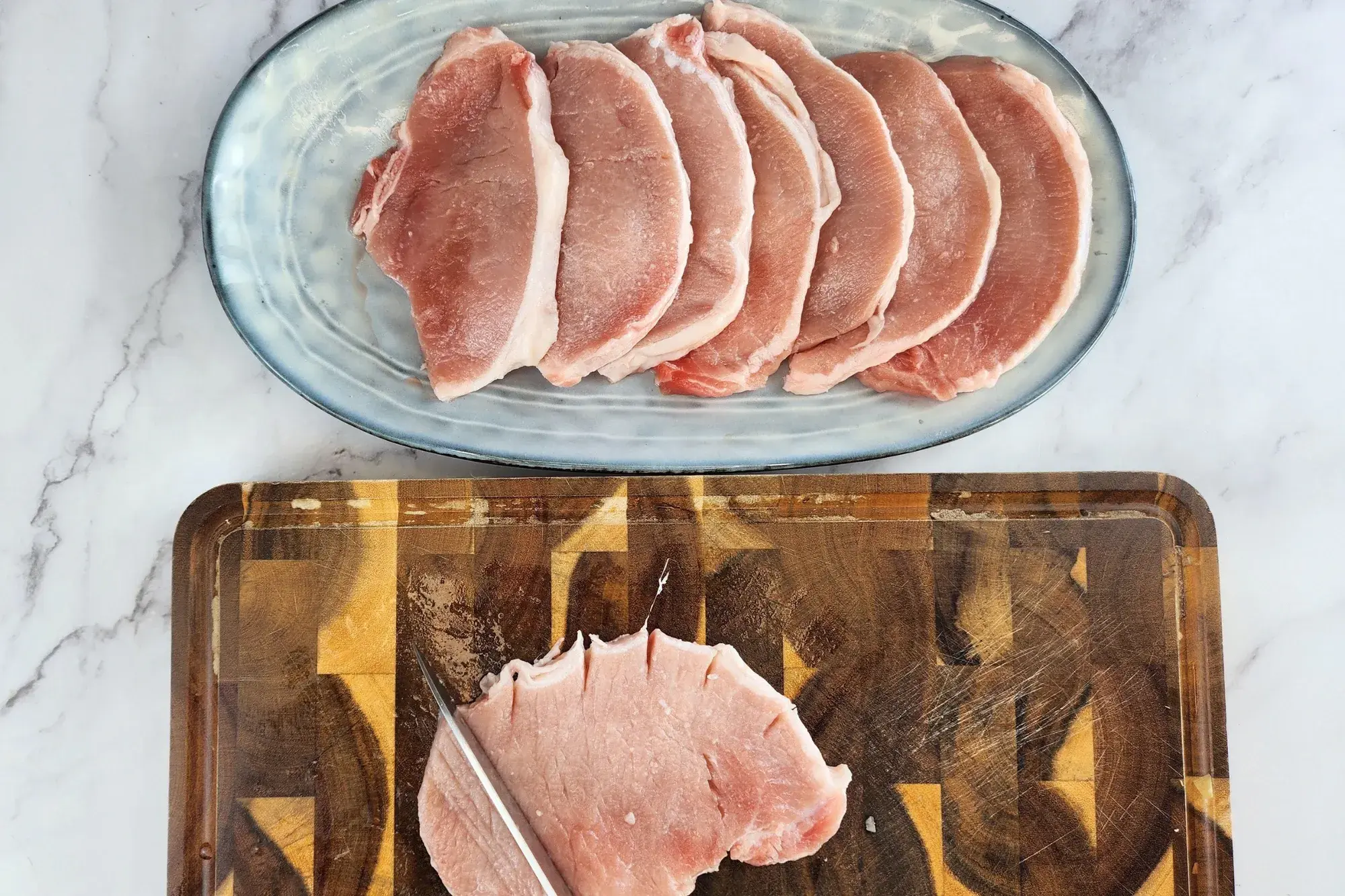 A knife cuts a pork chop on a chopping board next to a plate of pork chops