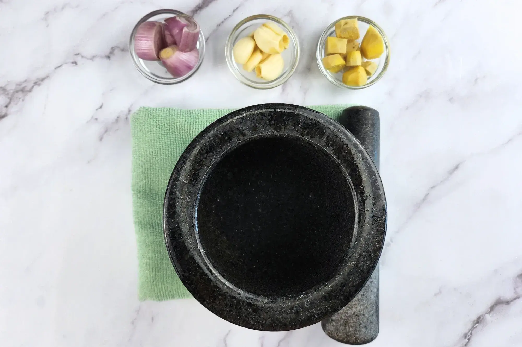 A mortar with three bowl of shallots, garlic and ginger.